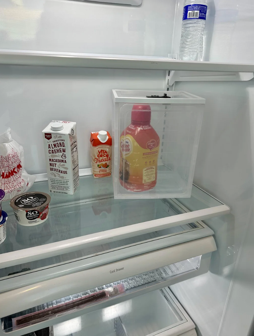 Open refrigerator with drinks, including almond milk, vitamin C juice, and a half-full juice container in a clear box