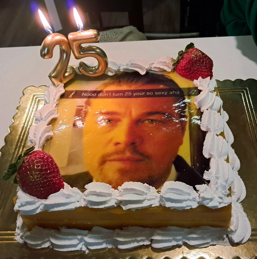 Birthday cake with strawberries, whipped cream, and a photo of a man's face. Number 25 candles are lit on top