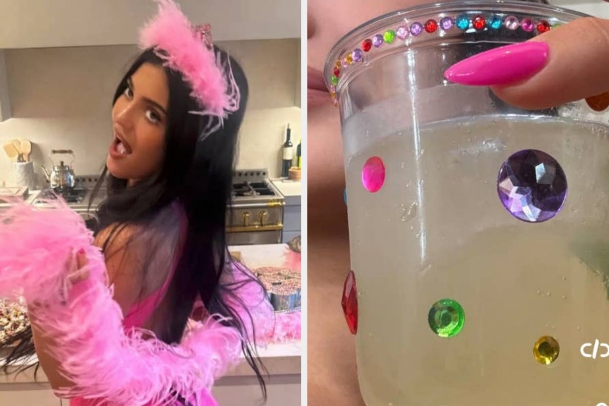 Person in a kitchen wearing a feathered accessory and tiara. Holds a jeweled cup with a drink. Playful and celebratory pose