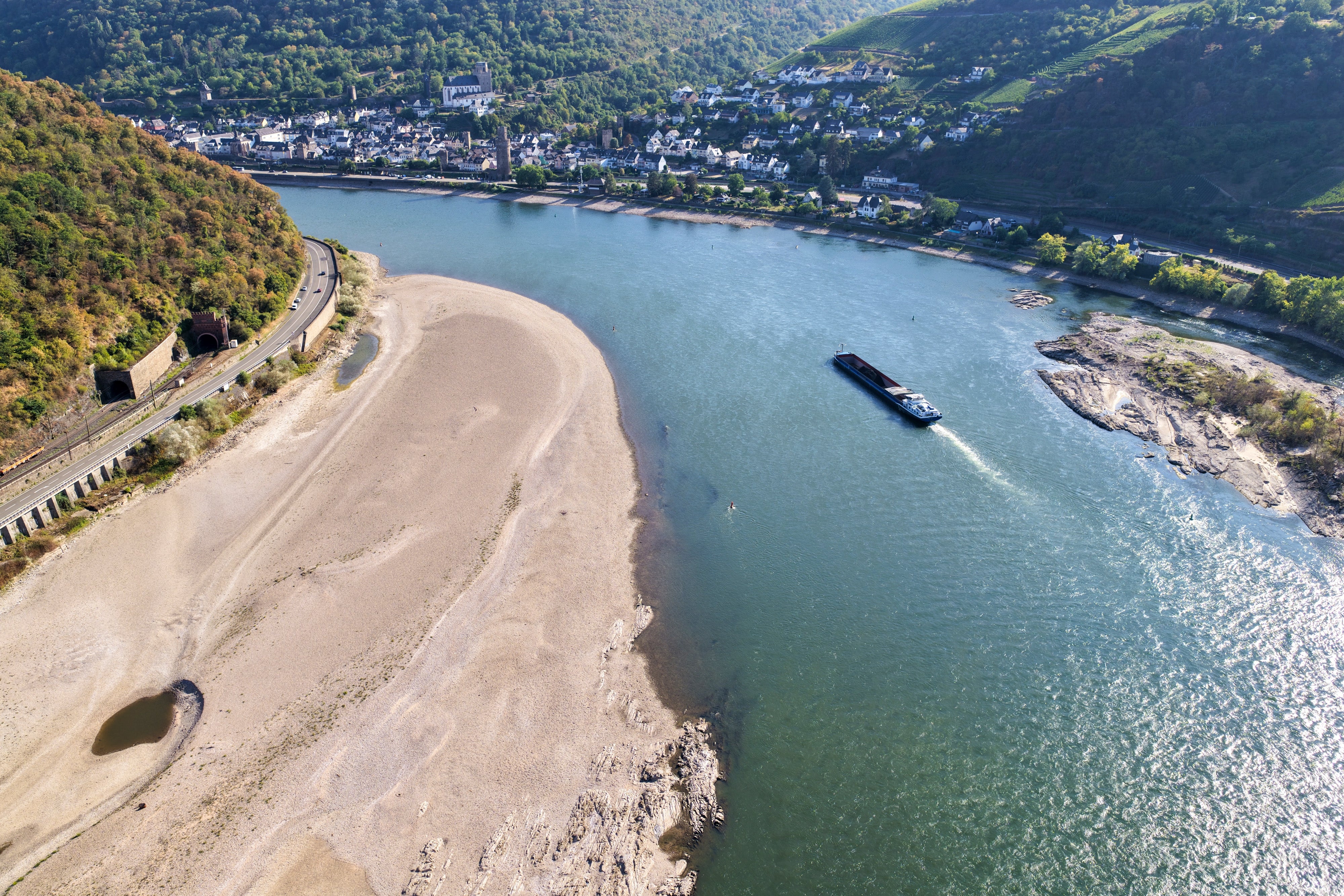 Luftfoto av en smal elv som slynger seg gjennom et kupert landskap med en lekter som navigerer vannveien, i nærheten av et delvis tørt elveleie