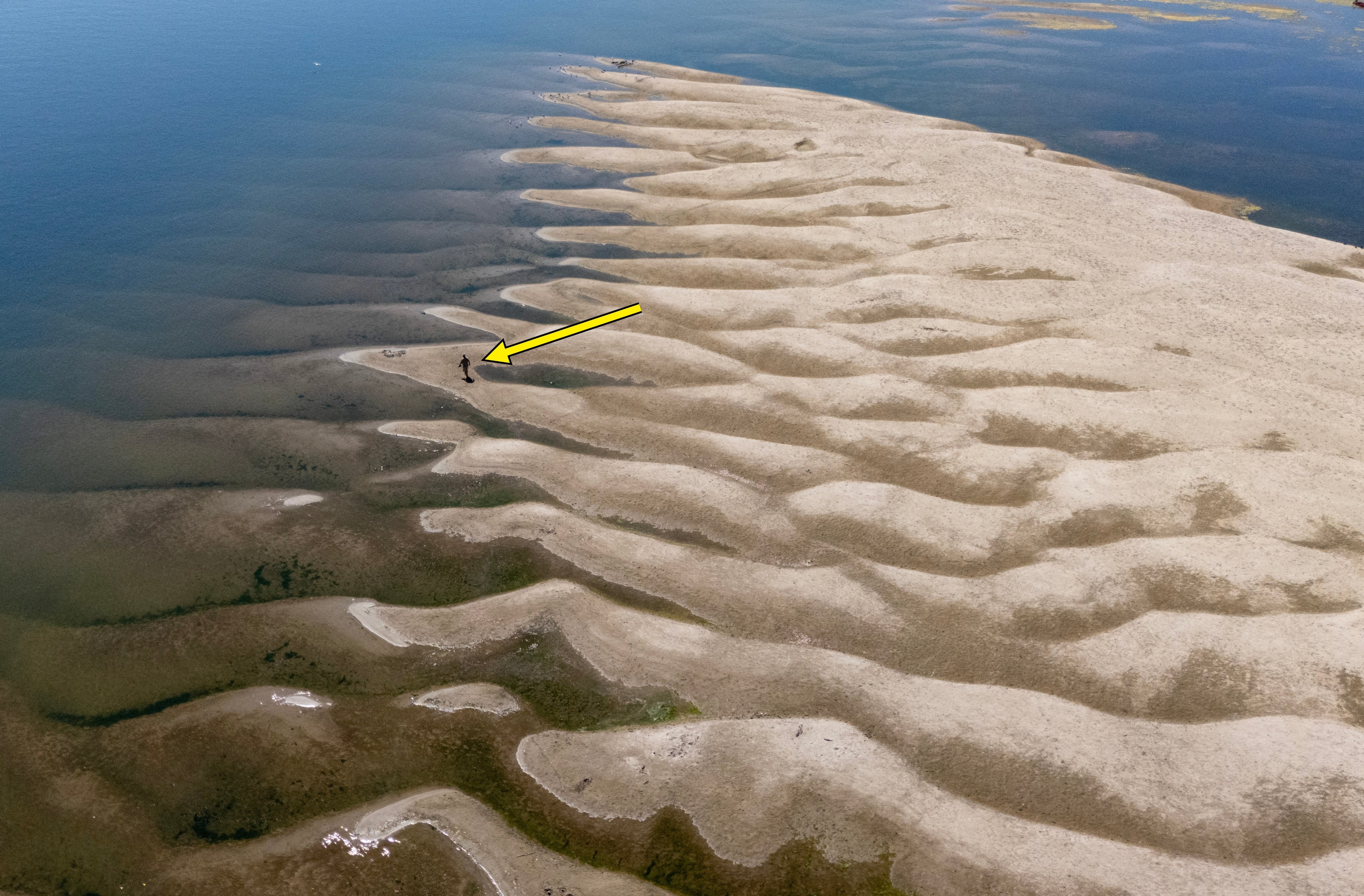 Luftfoto av krusede sandformasjoner langs en strandlinje, med vann som fyller mellomrommene. En person går i det fjerne