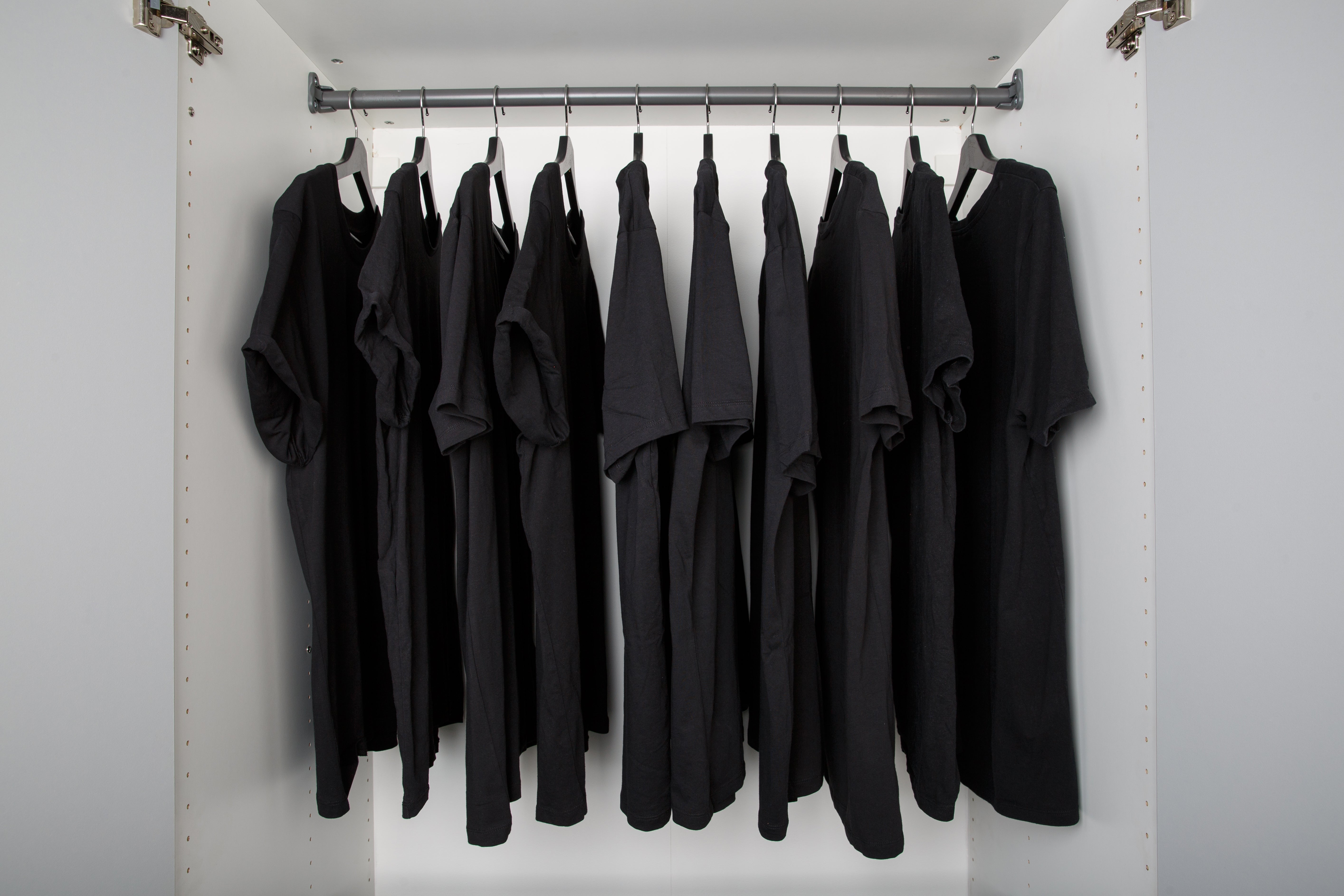 A closet with several identical black T-shirts neatly hanging on a rail