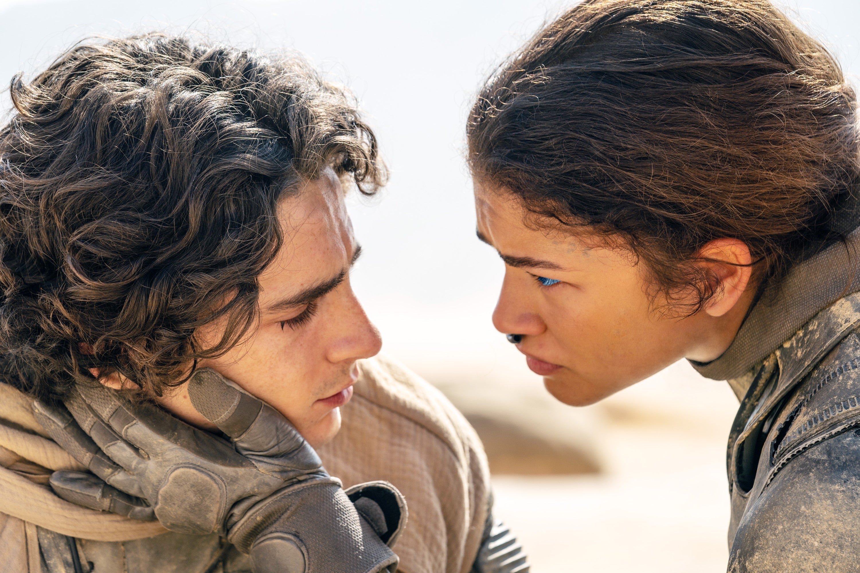 Two actors in a dramatic scene, one gently holding the other's face as they share an intense gaze. Both in elaborate sci-fi costumes
