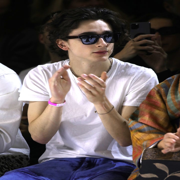 Person wearing sunglasses and a white t-shirt, sitting and clapping at an event