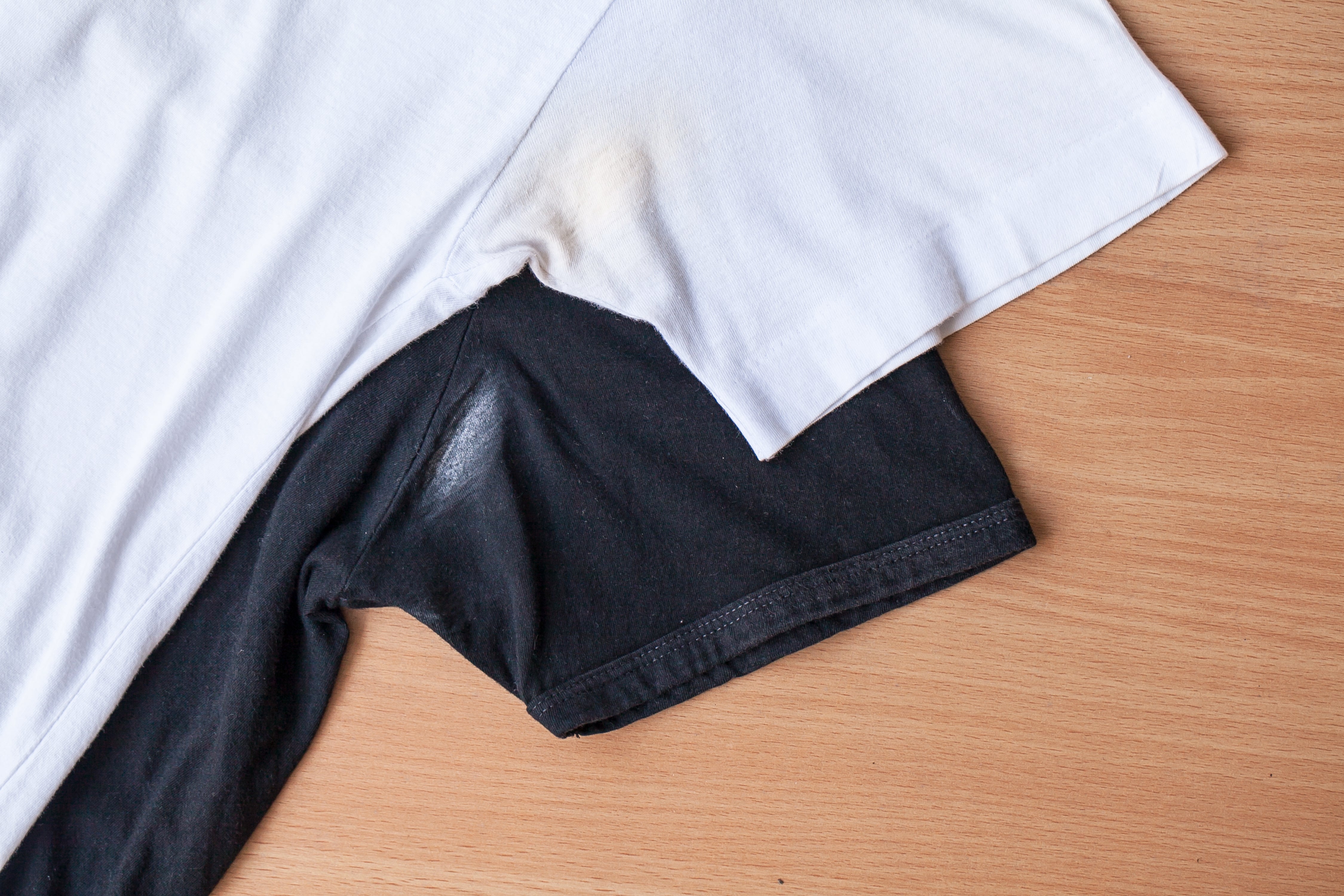 Two overlapping shirts, 1 achromatic and the different black, laid connected a woody surface, showing underarm stains connected both