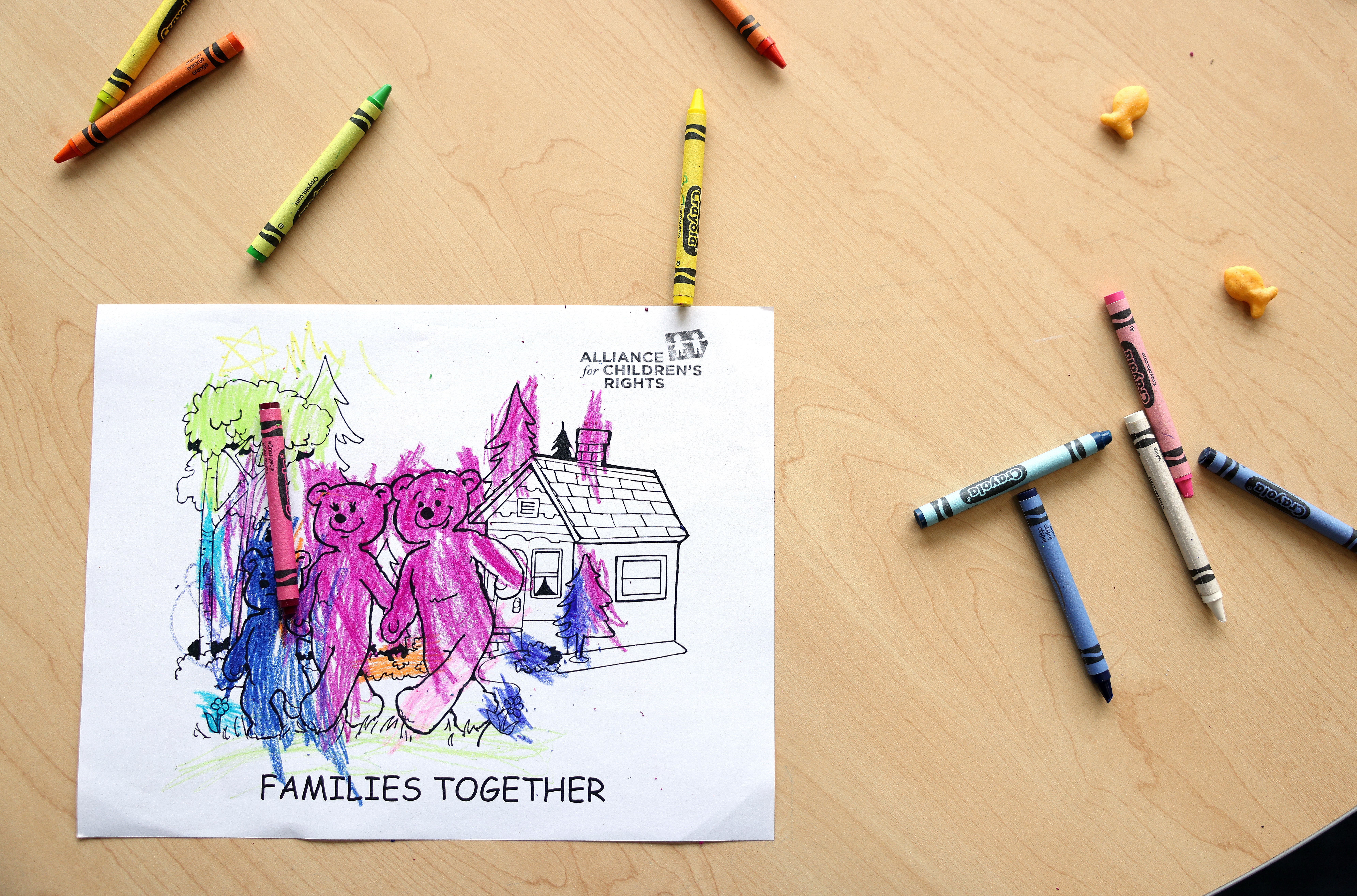 Children's coloring leafage with a house, trees, and 2 bears, titled "Families Together." Crayons and carnal erasers prevarication nearby