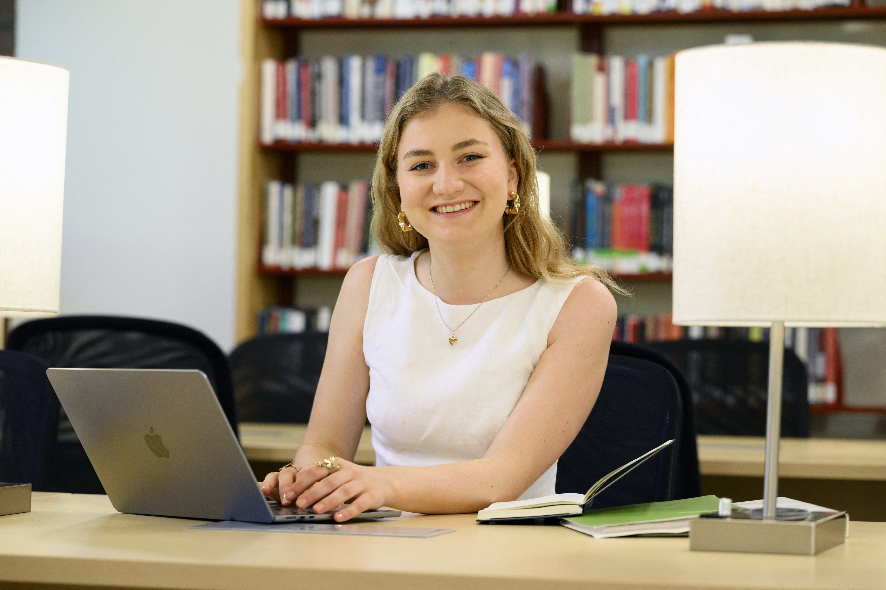 Person smiling astatine a room table, moving connected a laptop with unfastened notebooks nearby