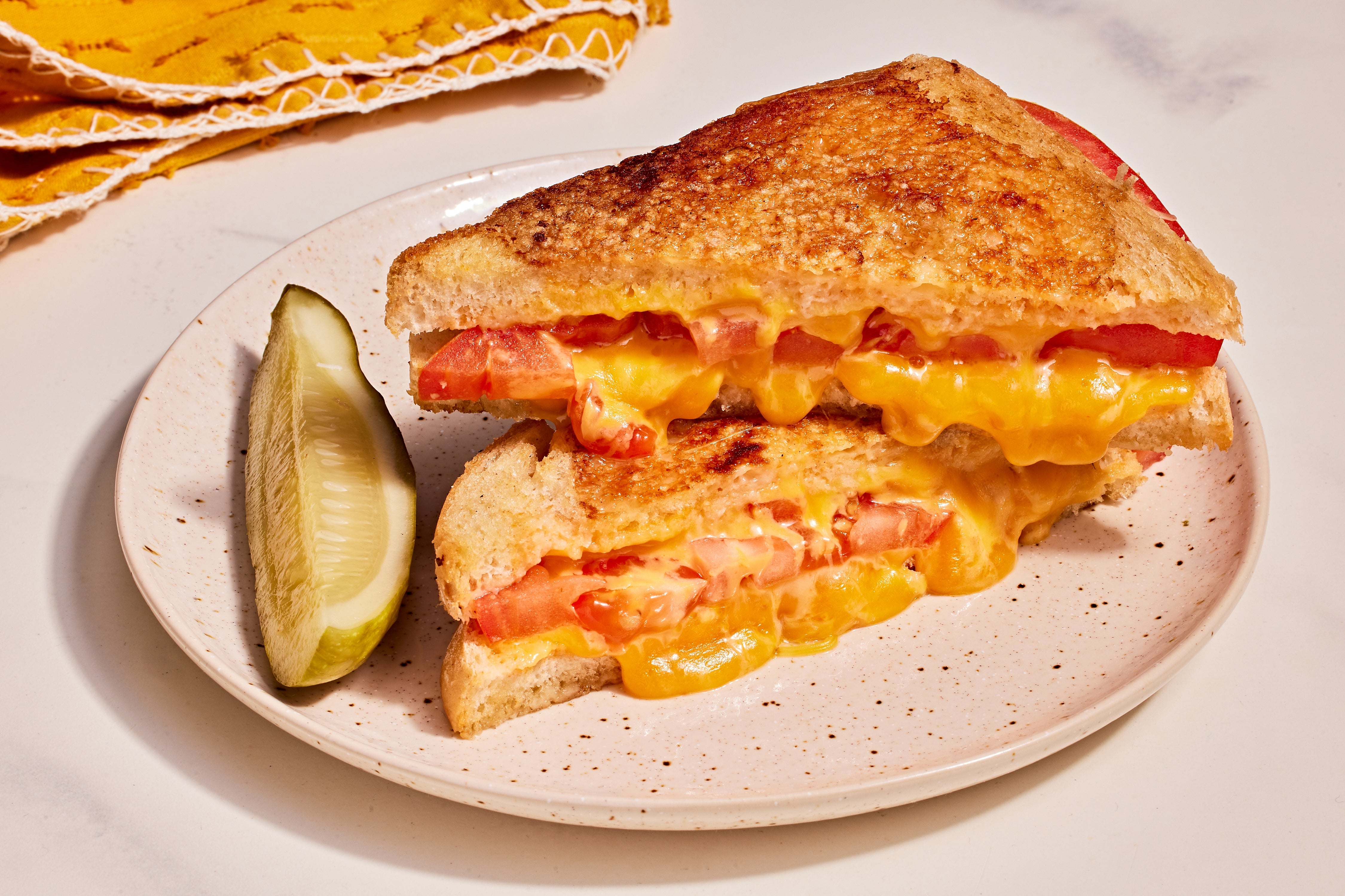 Grilled food sandwich with melted food and herb slices connected a plate, adjacent to a pickle wedge