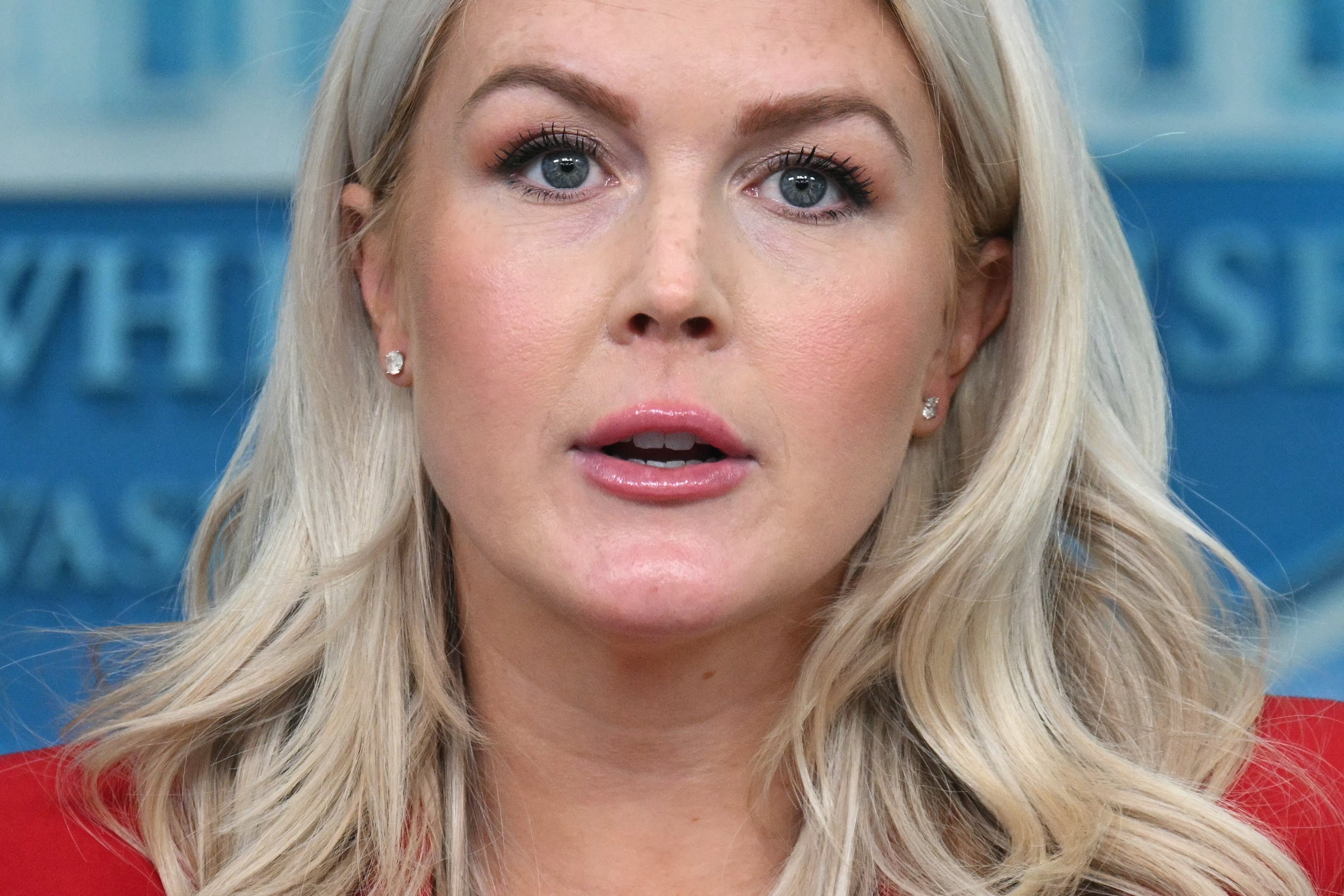 En person som snakker på et pressekonferansepodium, synlig bakteppe med offisielt emblem