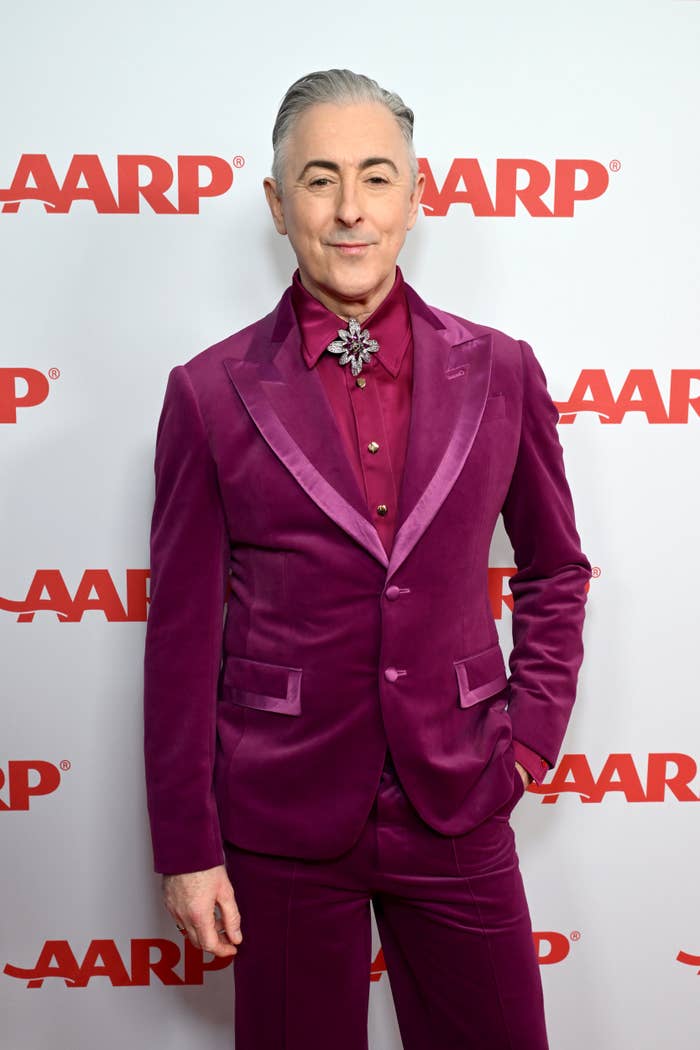 Person connected  the reddish  carpet wearing a velvet suit   with a floral bow tie
