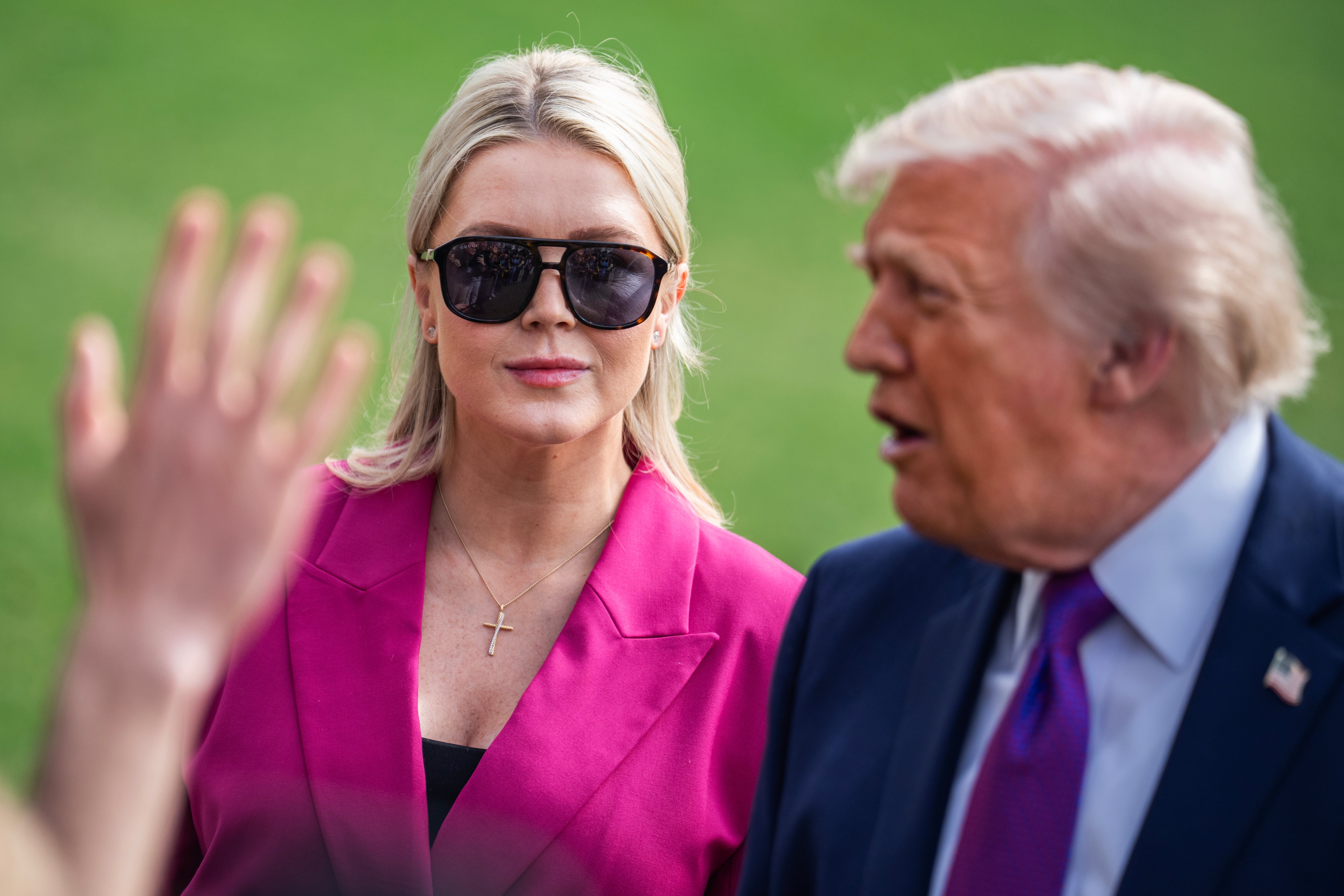To individer er utendørs; den ene har på seg solbriller og en rosa blazer, mens den andre snakker