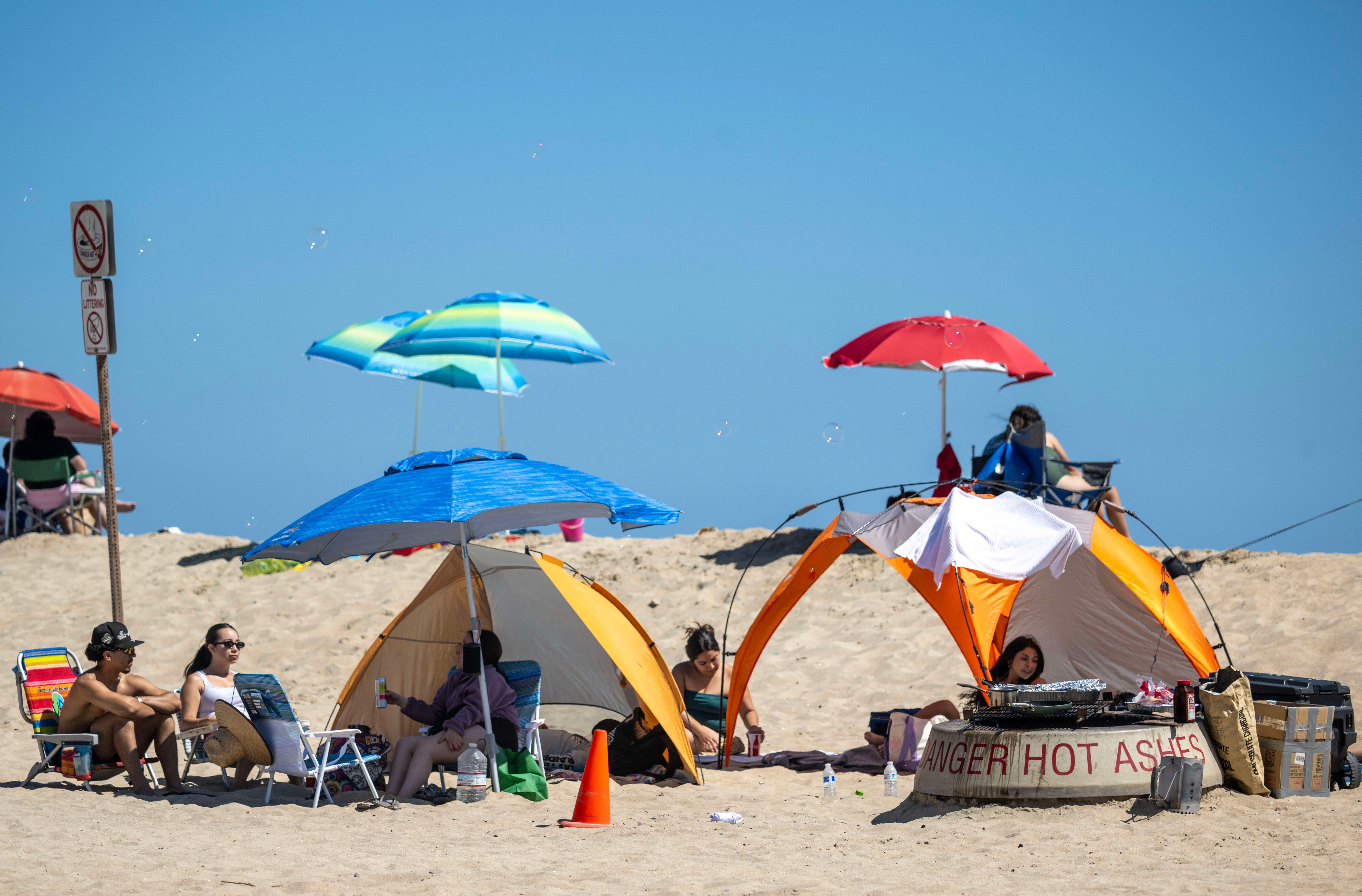 People relaxing nether umbrellas and tents connected a sunny beach, with a motion informing astir blistery ashes nearby