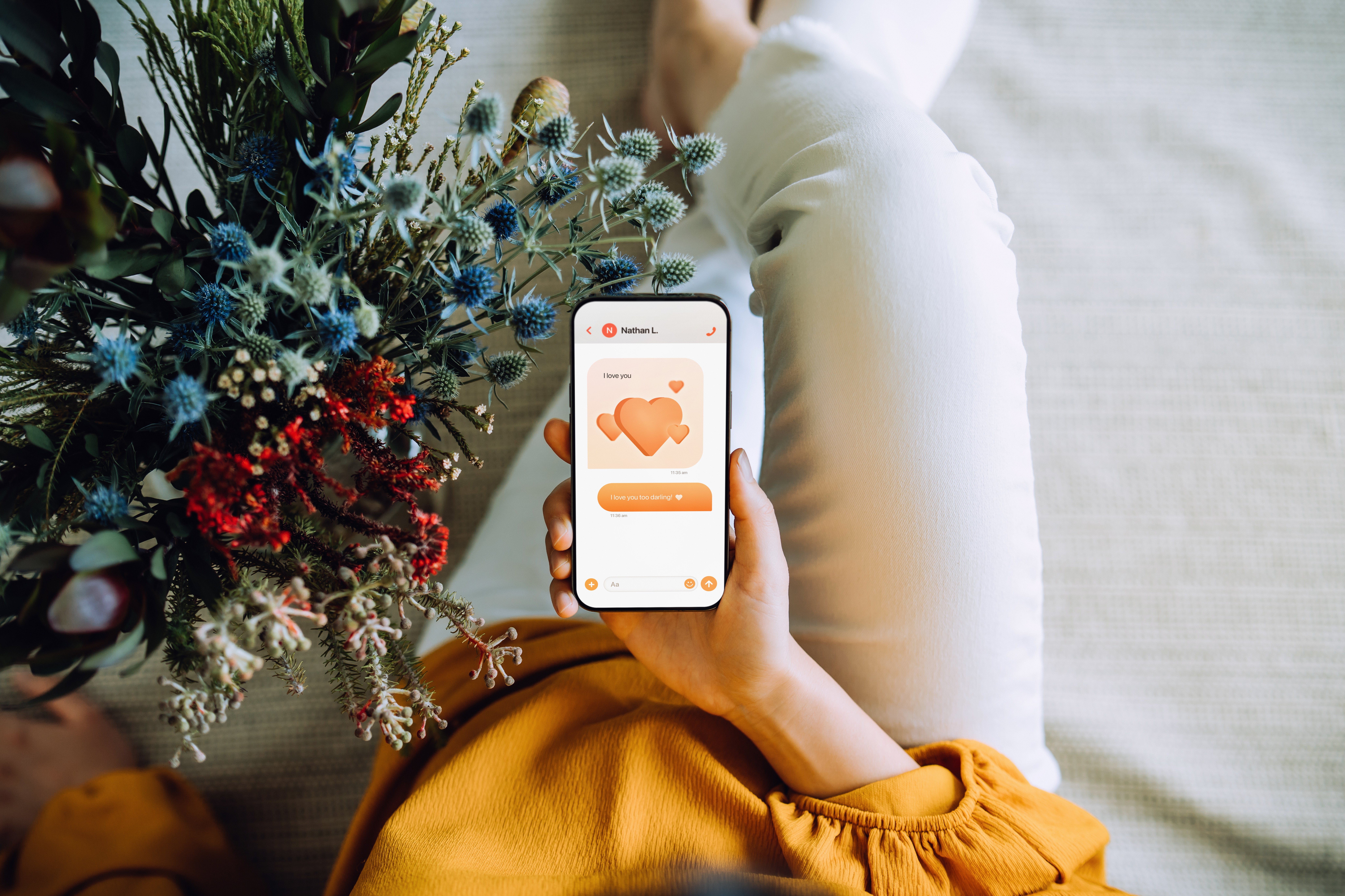 Person successful yellowish long-sleeve garment holds a bouquet and a smartphone showing a dating app with bosom icons