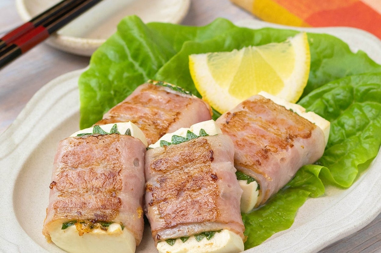 皿にレタスとレモンと一緒に並べられたベーコンで巻かれた豆腐の料理。