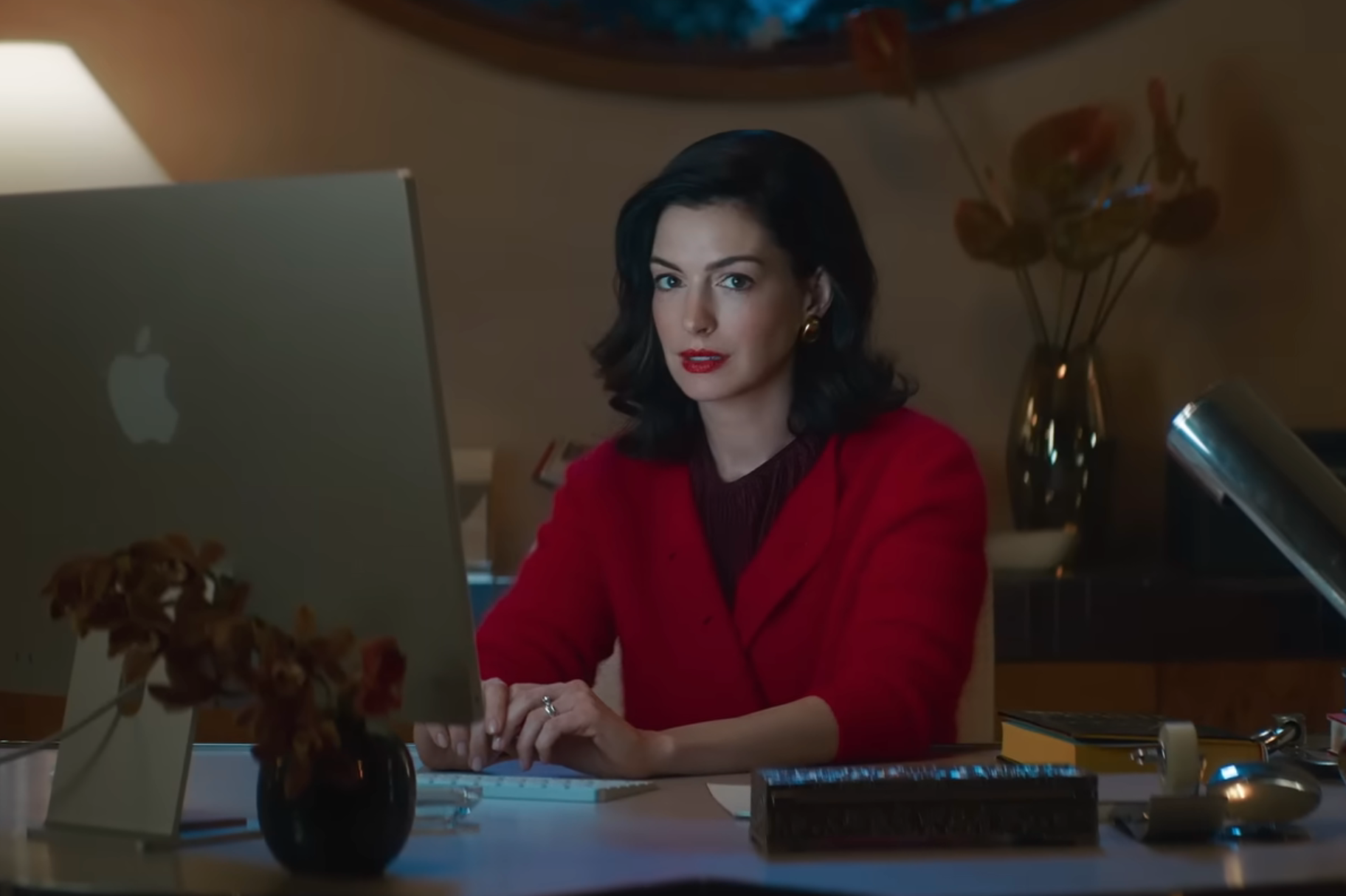 Person in a red blazer working at a computer in a stylish office setting, focused on the screen