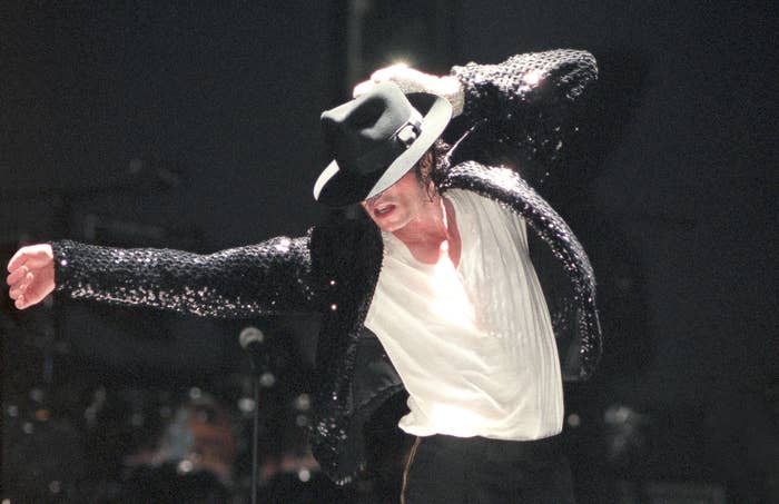 Performer in a sequined jacket, white shirt, and fedora, striking a dance pose on stage