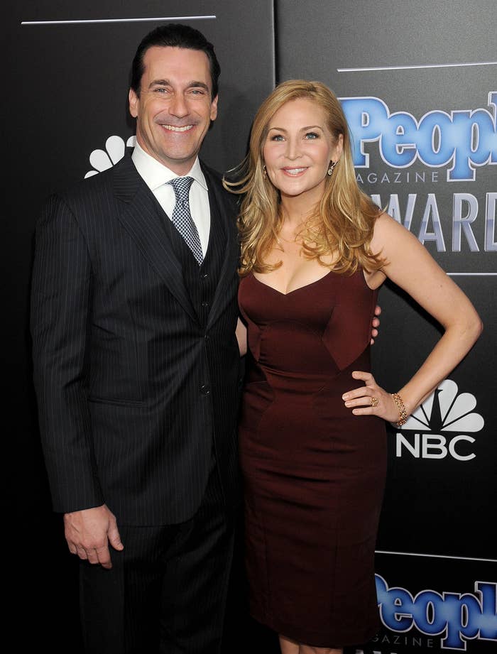 Man in a dark suit and tie with a woman in a fitted, strapless dress, posing on a red carpet at an awards event