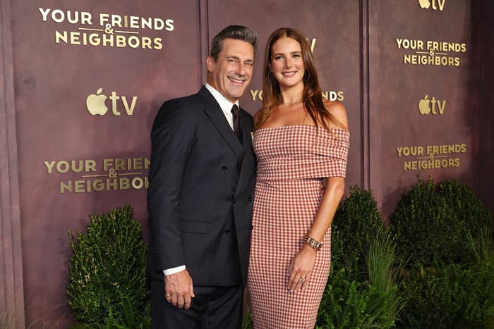 Two people smiling on a red carpet at an event for "Your Friends &amp;amp; Neighbors," wearing formal attire