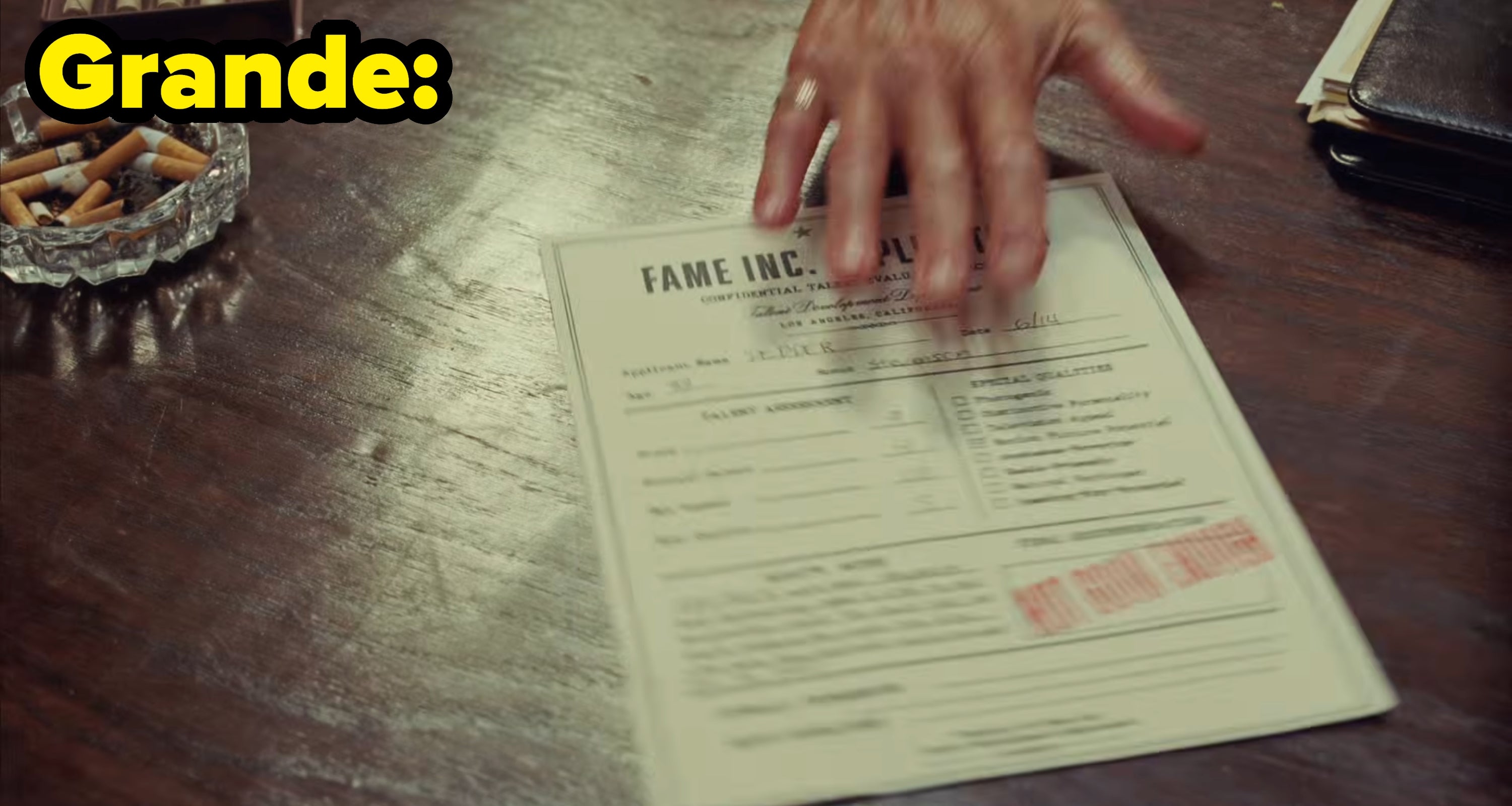 Grande's video, where a man slides a document on a table, labeled "Fame Inc" stamped with "Not good enough"