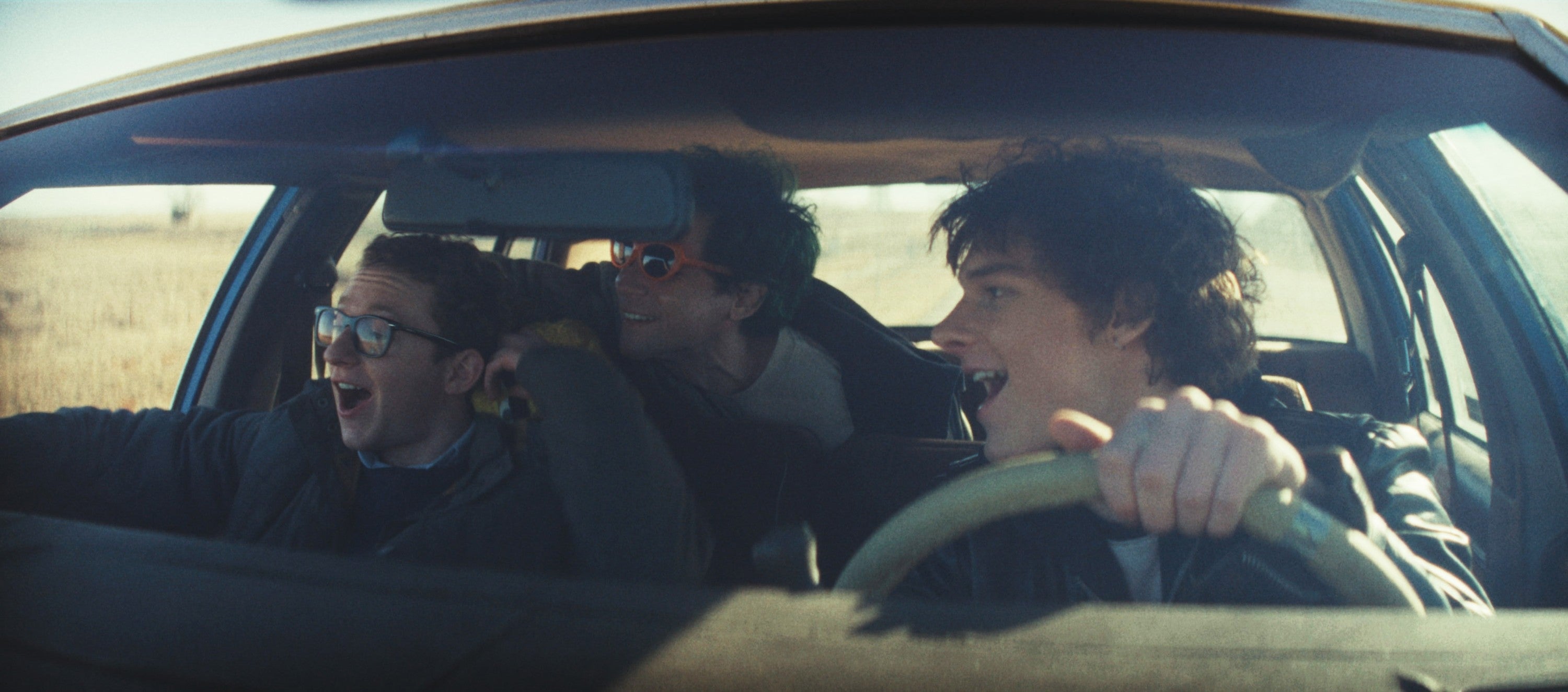 Three people joyfully ride in a car, the driver showing excitement