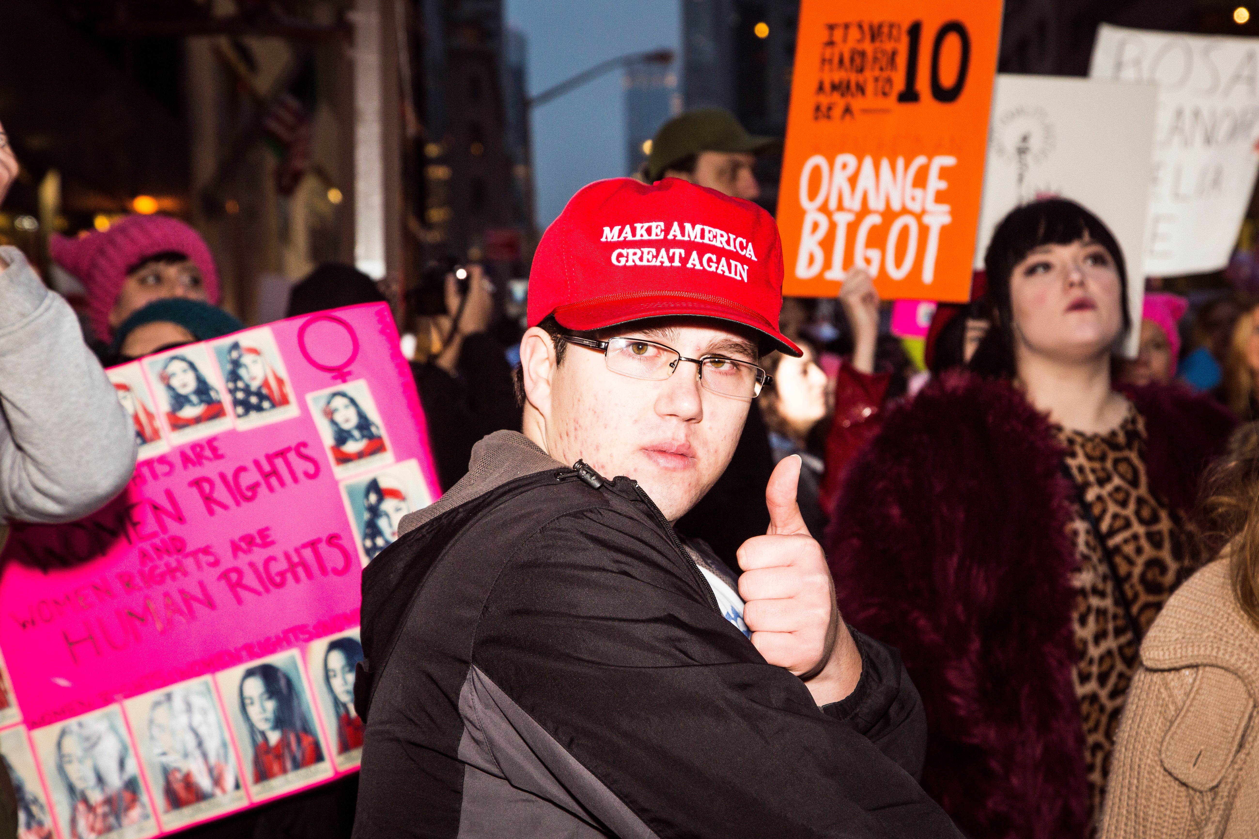Person som har på seg en "Make America Great Again" hatten gir tommel opp i en protestmengde. Tegn om kvinners rettigheter og politiske spørsmål er synlige