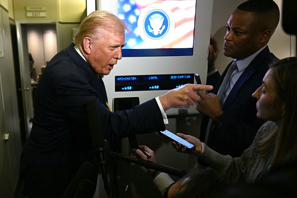 Donald Trump i en dress engasjert i samtale med journalister på et fly, og gestikulerer ettertrykkelig med en finger