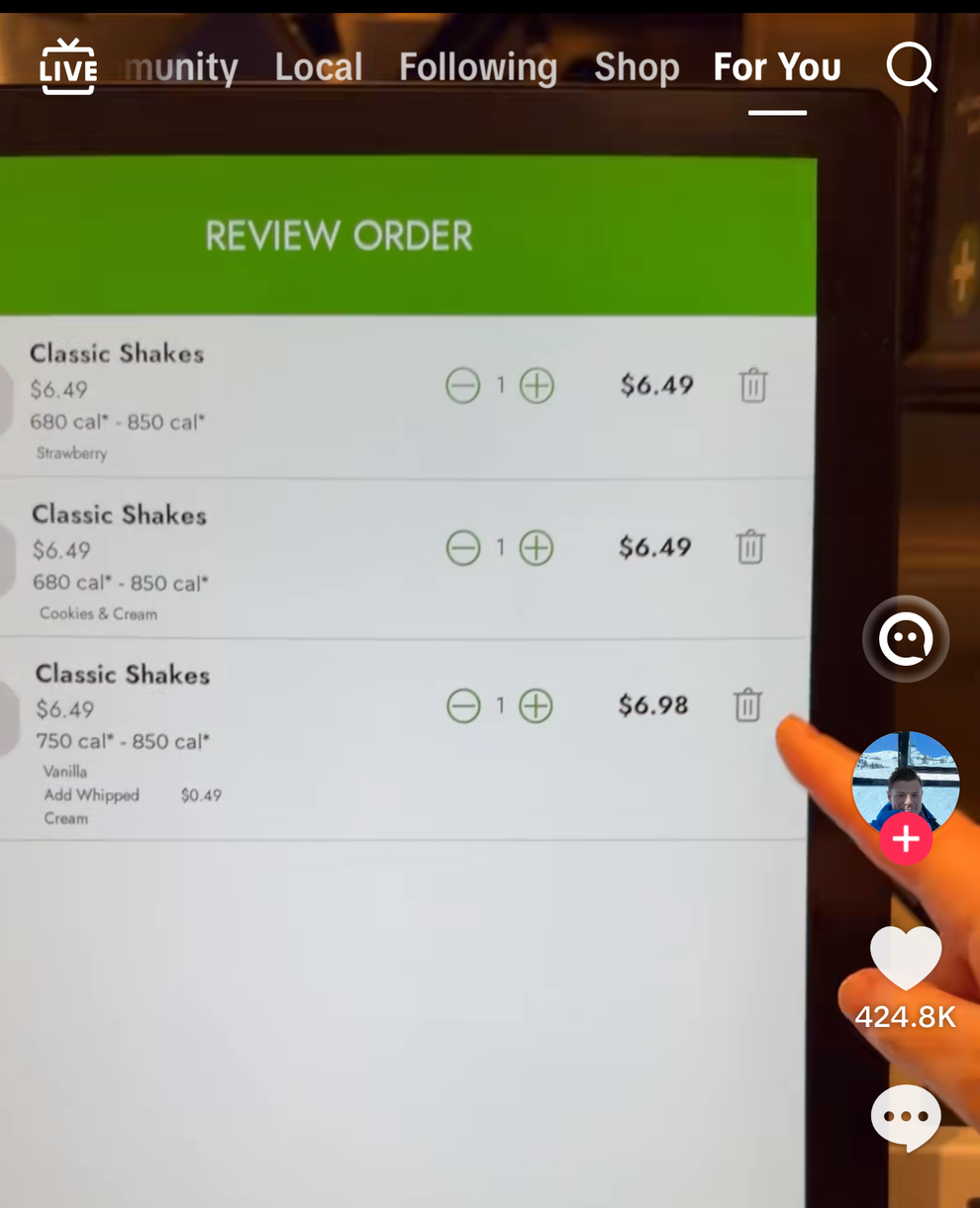 A digital order screen showing three classic shakes listed with prices and calorie counts. A hand with red nails points to the screen