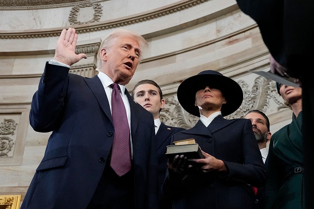 Donald Trump står med løftet hånd, avlegger en ed, ved siden av Melania Trump i frakk og bredbremmet hatt, og holder en bok