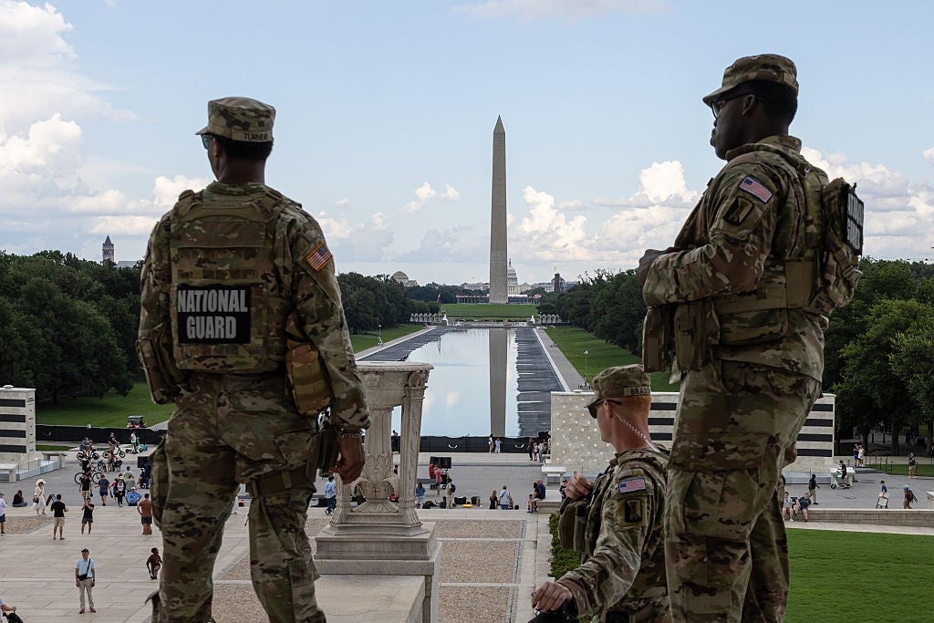 Tre nasjonalgardesoldater i kamuflasje står med utsikt over Lincoln Memorial Reflecting Pool med Washington-monumentet i bakgrunnen