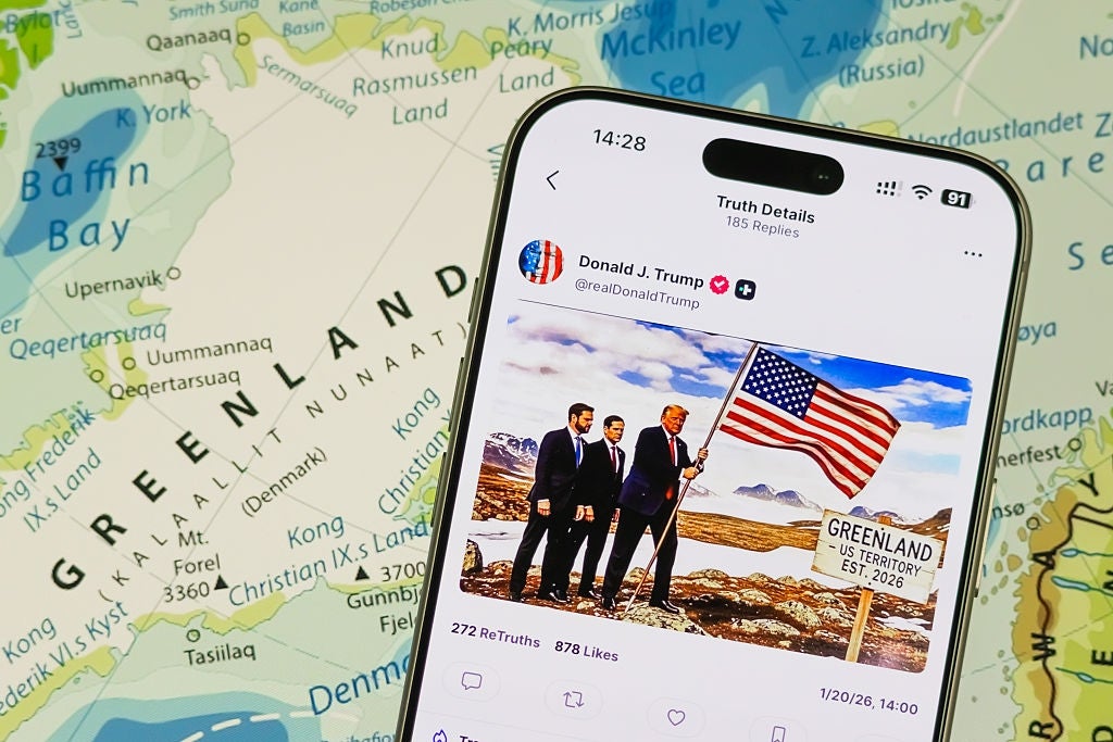 En smarttelefon viser et innlegg på sosiale medier av tre politikere som holder et amerikansk flagg ved siden av et 
