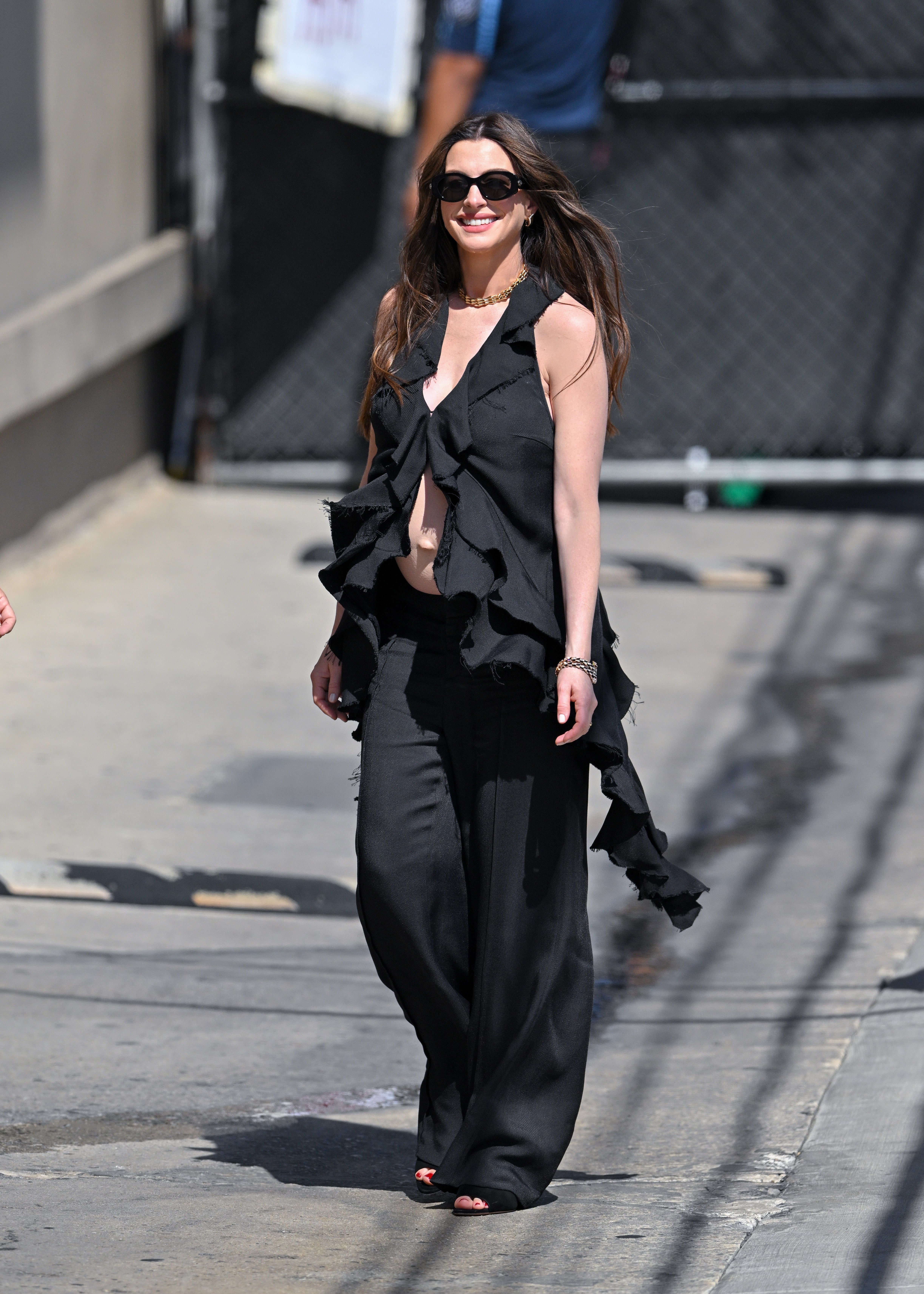 Celebrity in stylish, flowing black ensemble with sunglasses, walking outdoors