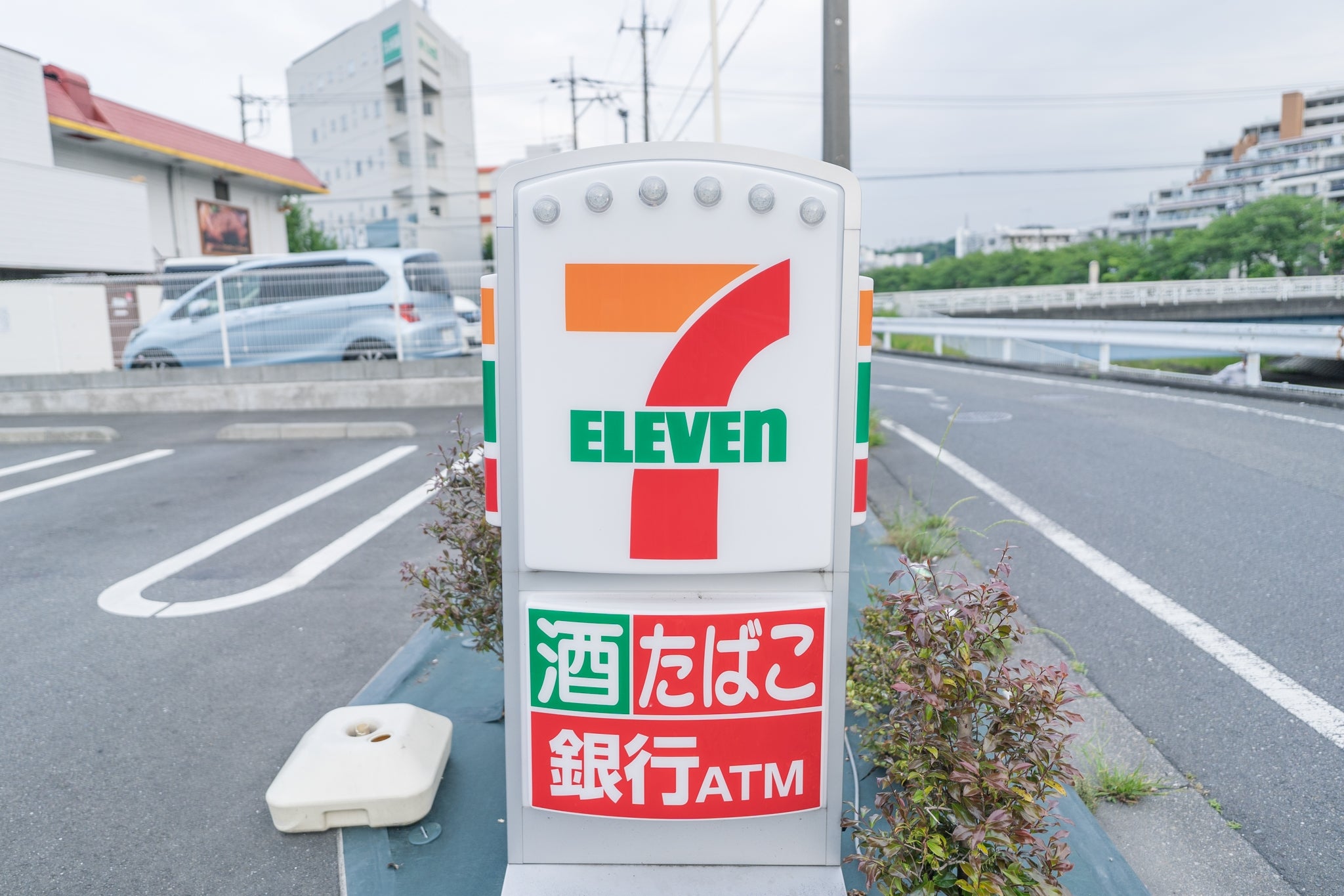 7-Eleven駐車場の看板には、「酒、たばこ、銀行ATM」の文字が表示されています。