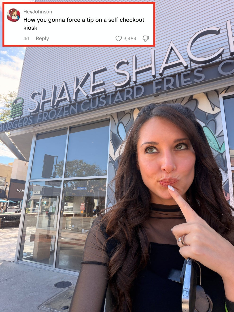 Person with long hair playfully poses outside Shake Shack with a thoughtful expression, touching their chin