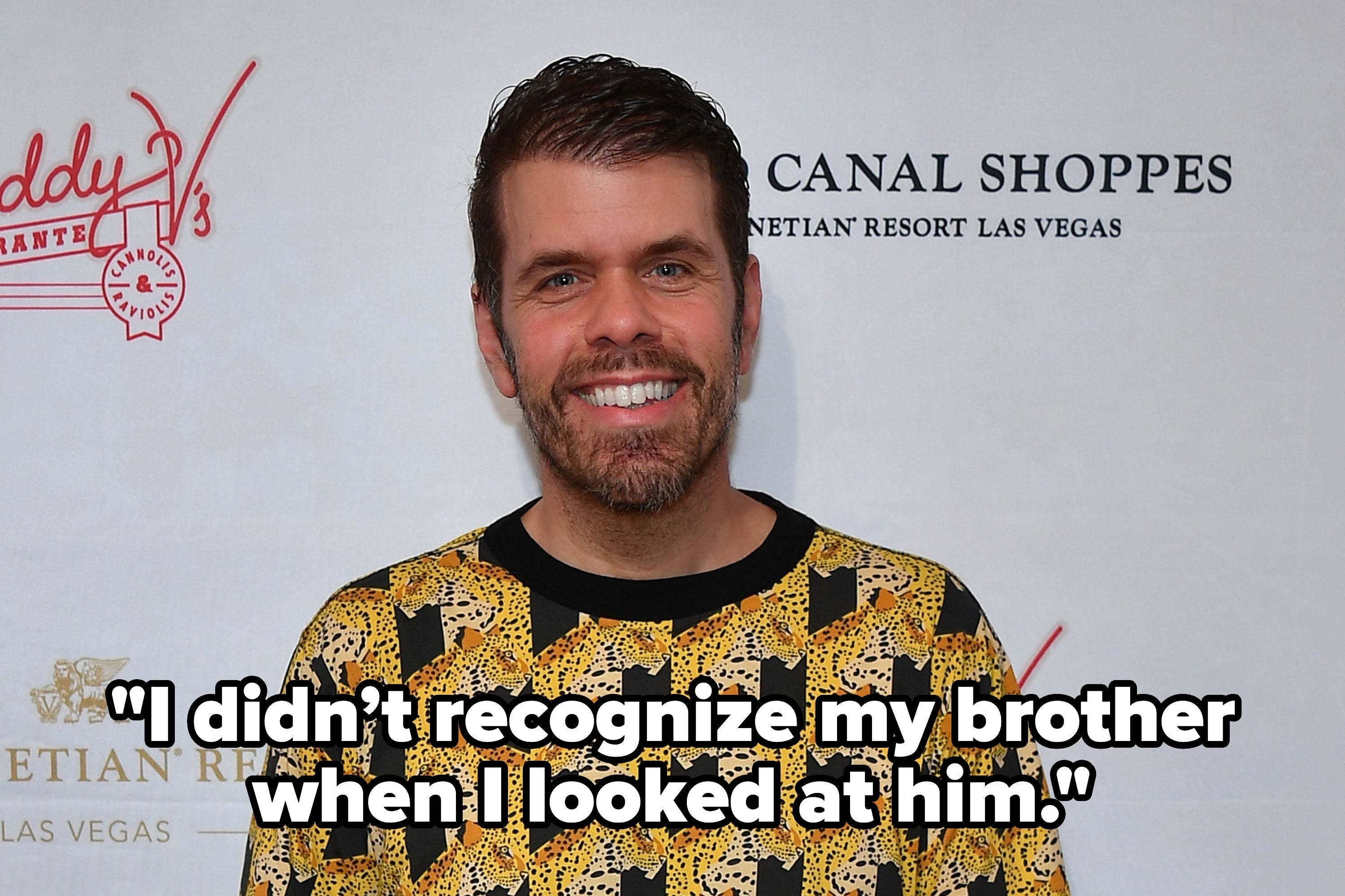 Person in patterned shirt poses on a step and repeat backdrop at a celebrity event