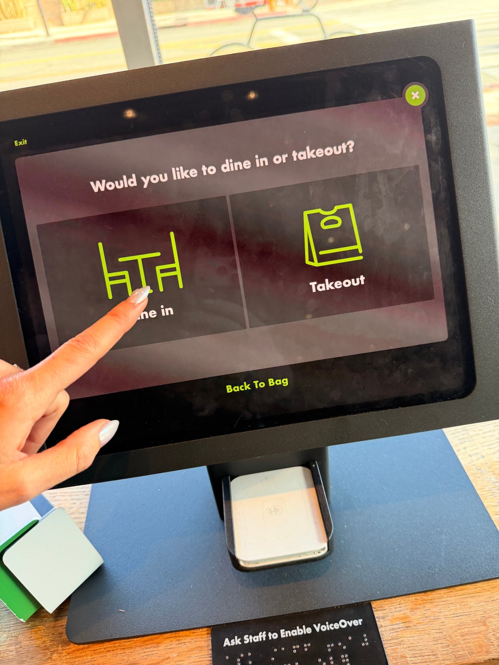 A person selects the "Dine in" option on a touchscreen displaying "Would you like to dine in or takeout?"