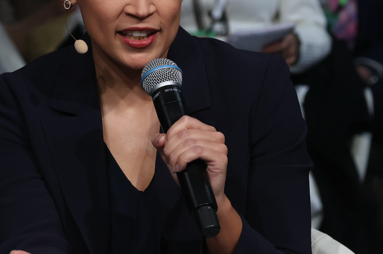Person speaking in a panel discussion, wearing a formal suit, holding a microphone, with attentive audience members in the background