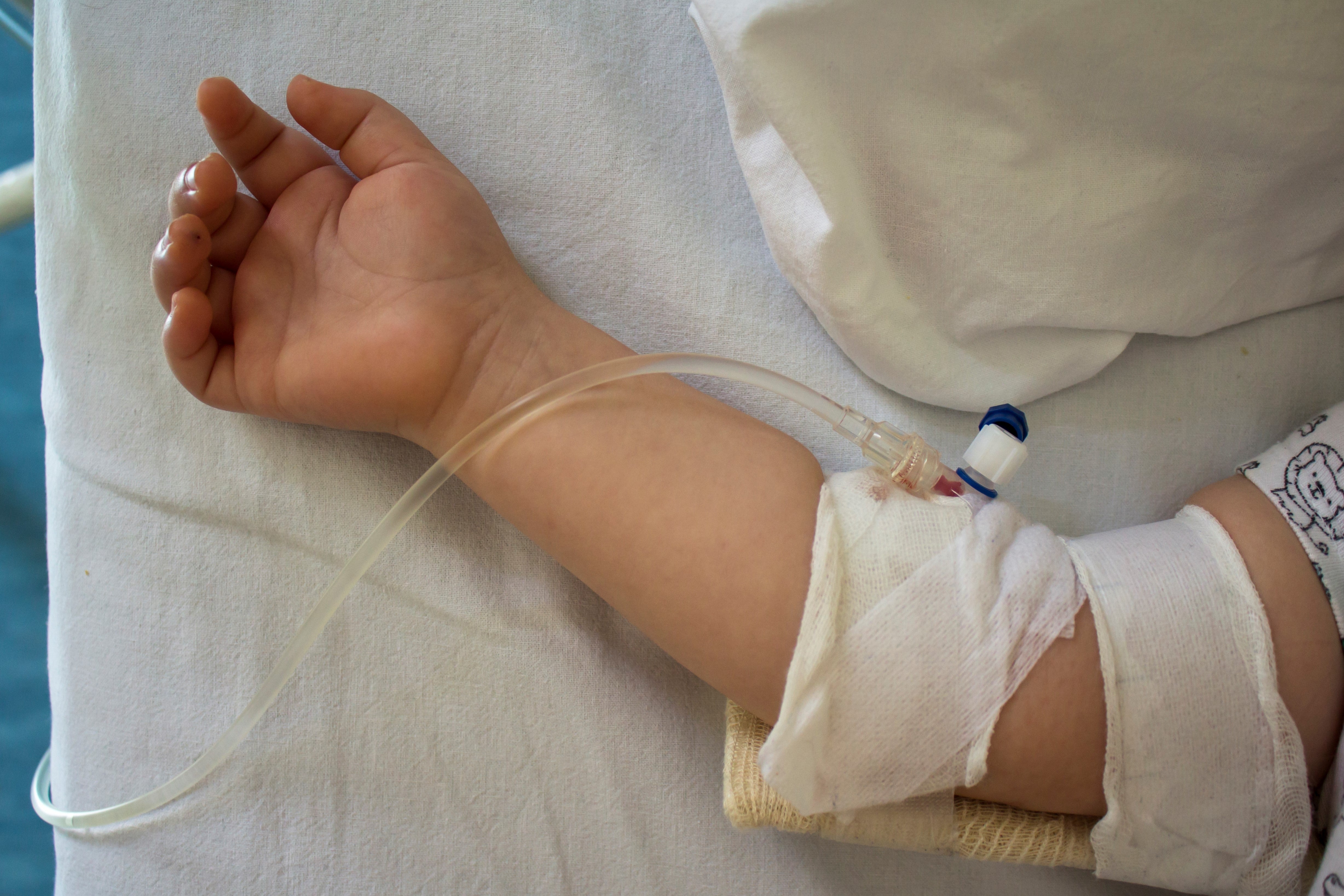 Barnearm med en IV-slange satt inn, hviler på en sykehusseng, som indikerer en medisinsk setting