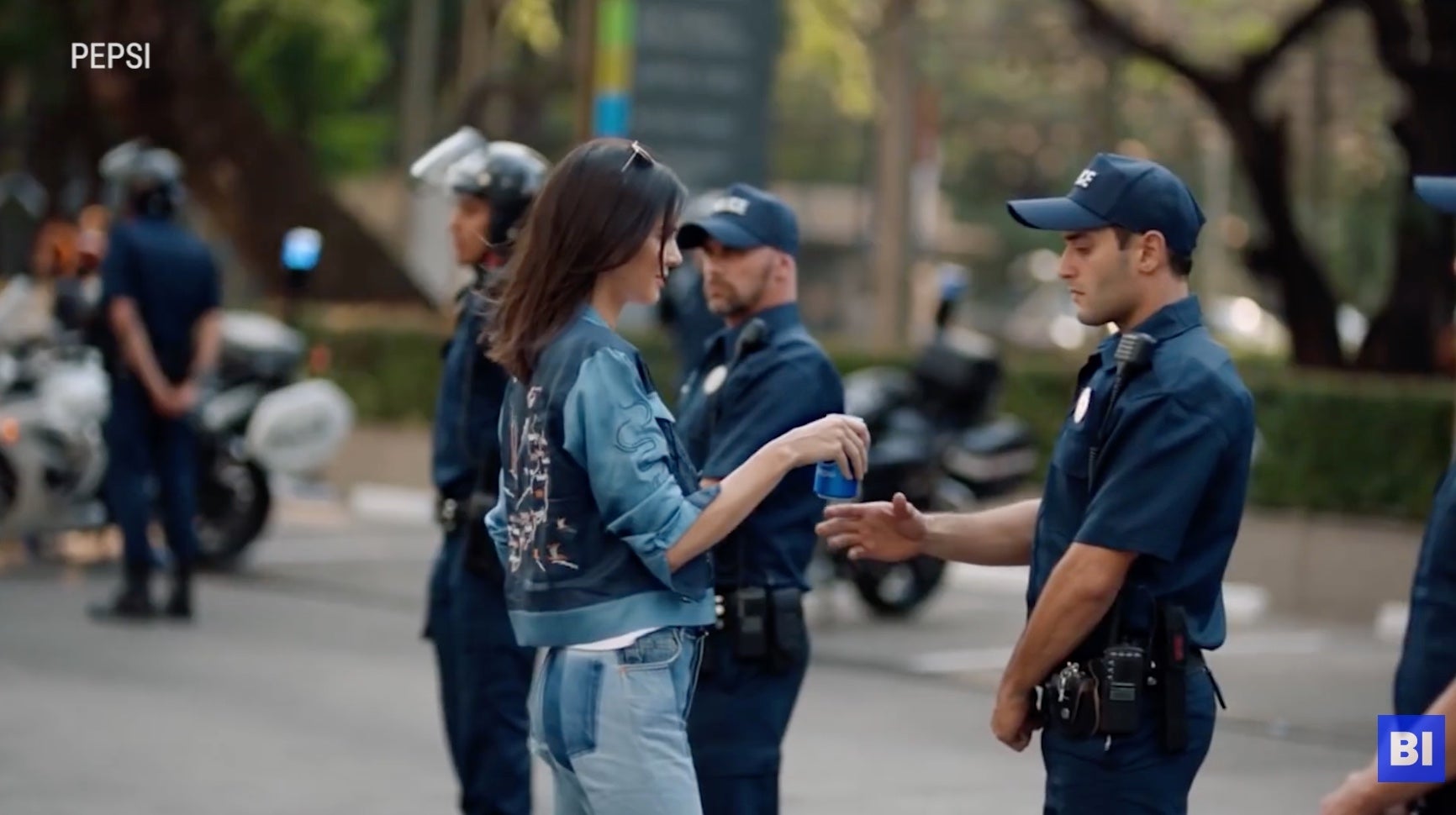Kendall Jenner hands a Pepsi can to a police officer in uniform in the midst of a protest