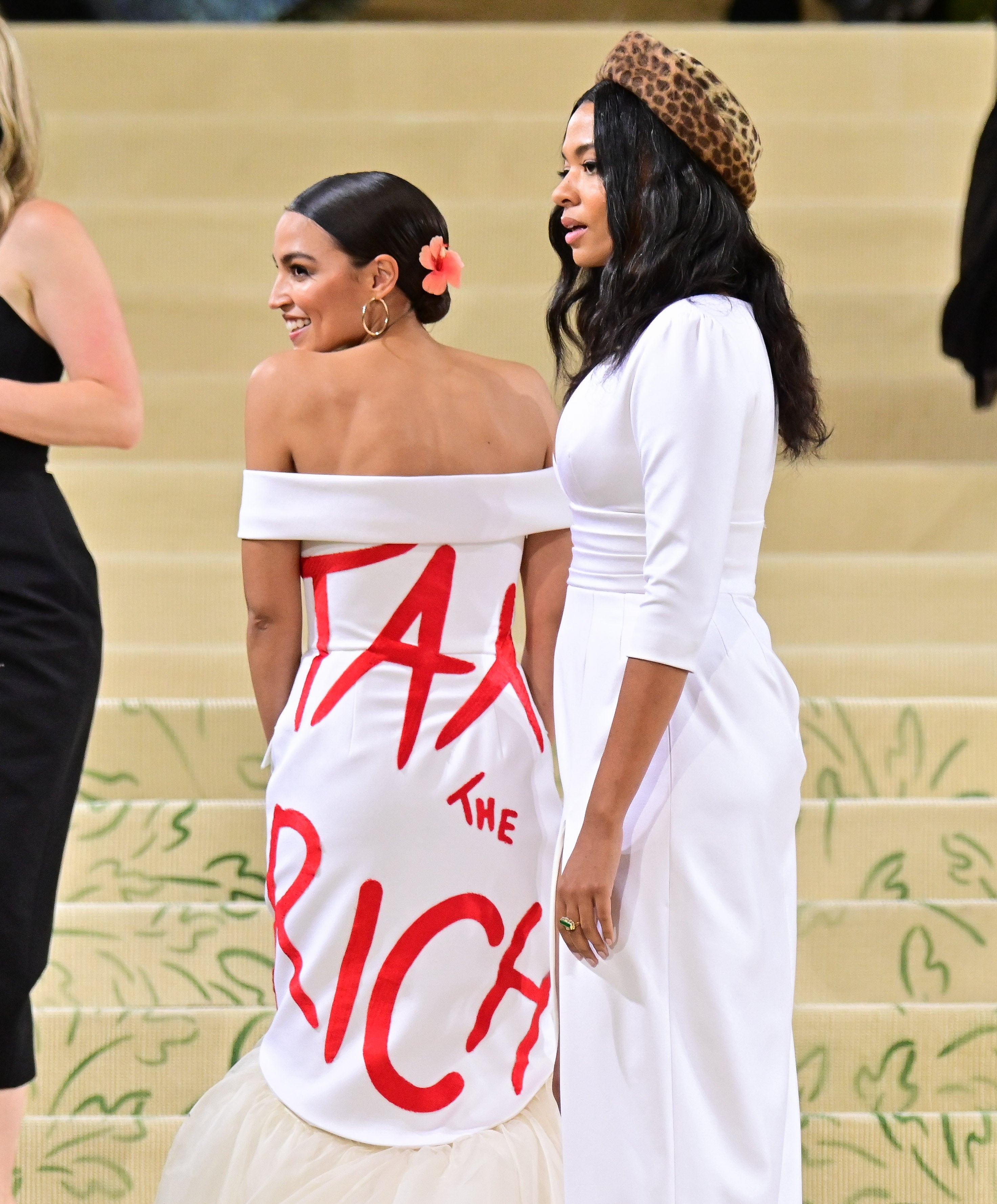 Alexandria Ocasio-Cortez at the Met Gala, wearing an off-shoulder gown with "Tax the Rich" written in bold red text.