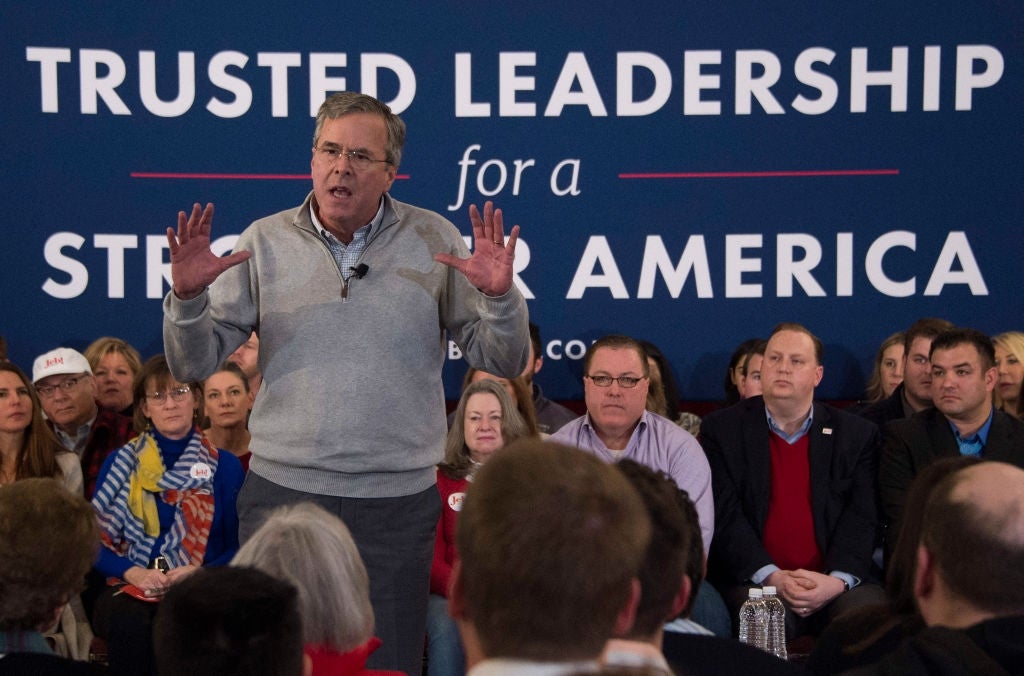 Jeb Bush snakker lidenskapelig på scenen med publikum sittende bak, foran et banner med teksten