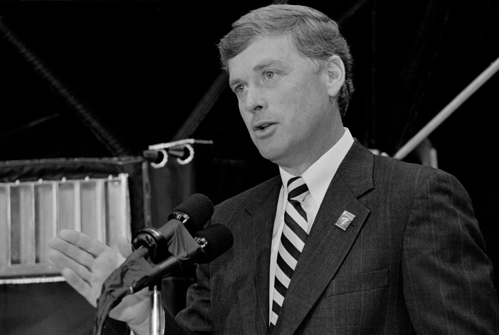 Dan Quayle i dress og slips snakker ved et podium med mikrofoner, gestikulerer med hånden, henvender seg tilsynelatende til et publikum eller presse