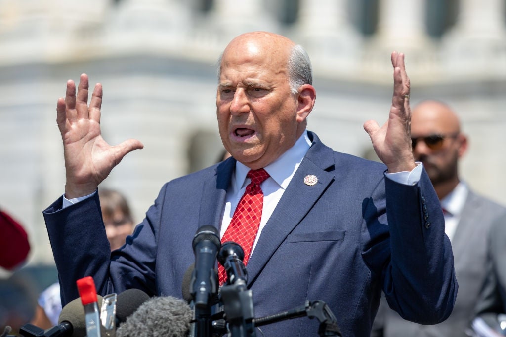 Louie Gohmert i dress og slips snakker lidenskapelig ved et podium omgitt av mikrofoner utendørs, med tilskuere i bakgrunnen