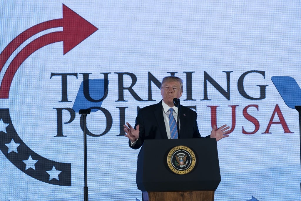Donald Trump på et podium med presidentseglet, taler på et Turning Point USA-arrangement