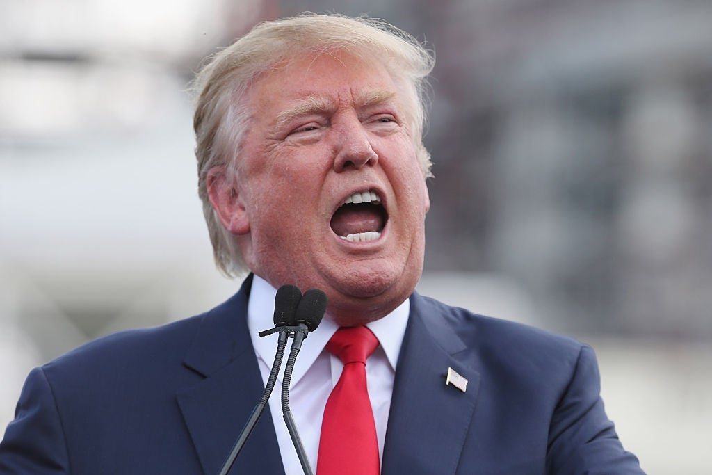 Donald Trump i dress og slips snakker lidenskapelig på et offentlig arrangement med mikrofoner foran seg
