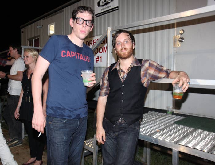 Patrick Carney and Dan Auerbach of The Black Keys stand outside a dressing room while holding drinks in their hands