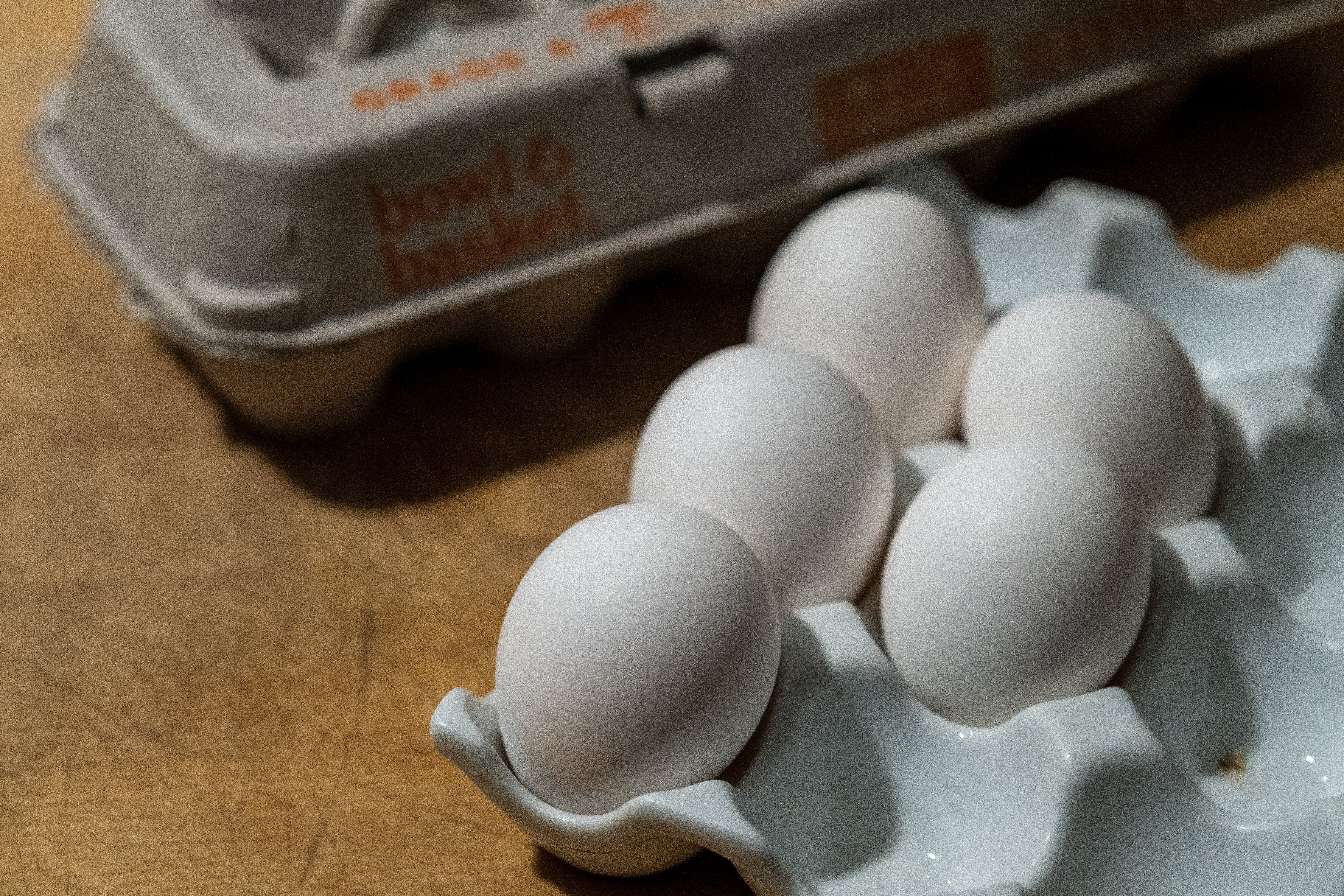 Egg i en kartong og et brett på en treoverflate, med merket "bowl & kurv" synlig på kartongen