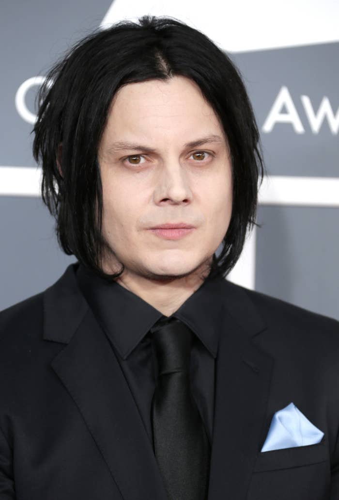 Jack White wears a dark suit with a blue pocket square at an event, standing against a grey backdrop