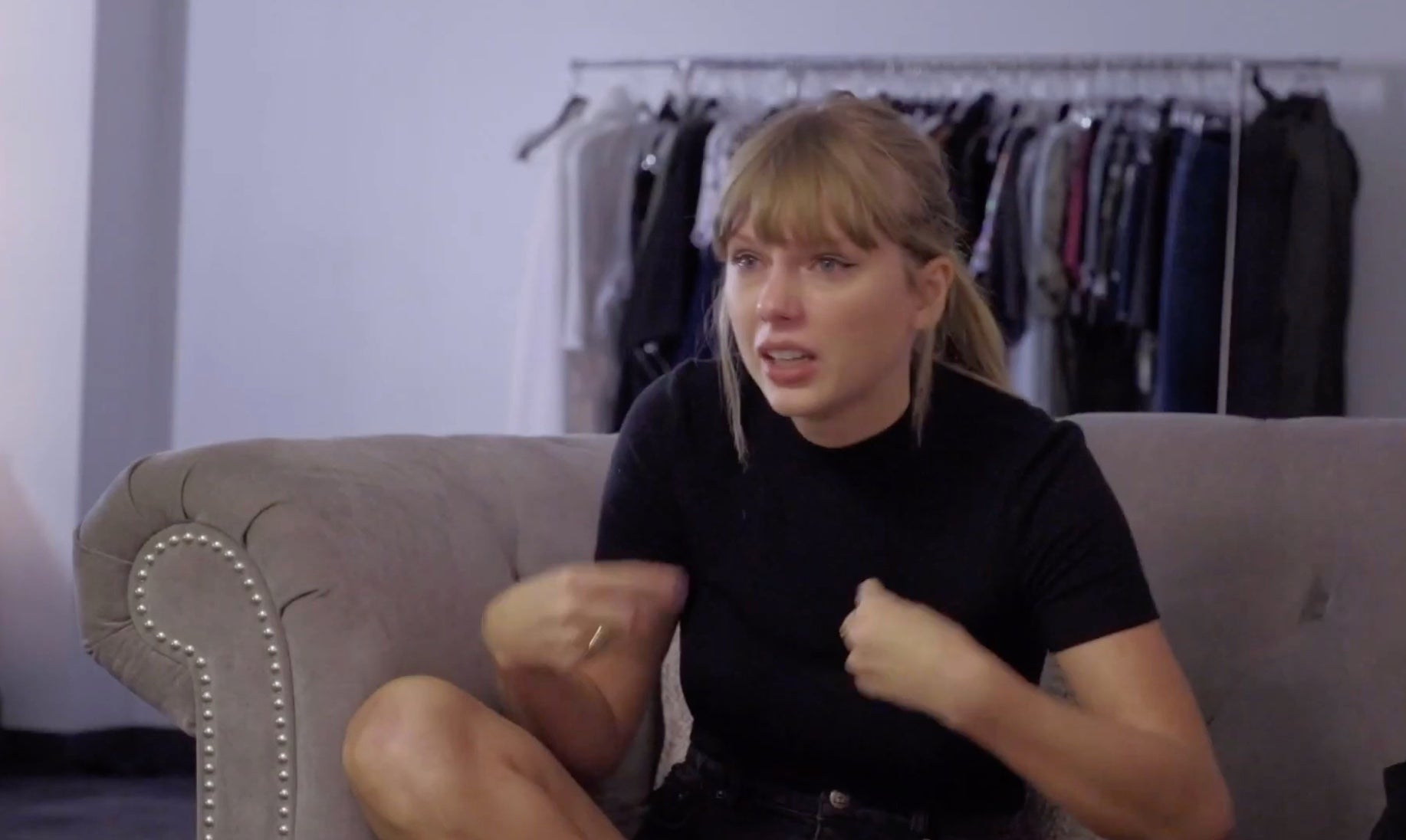 Taylor Swift sits on a couch while speaking to her team, emotionally voicing her political convictions.