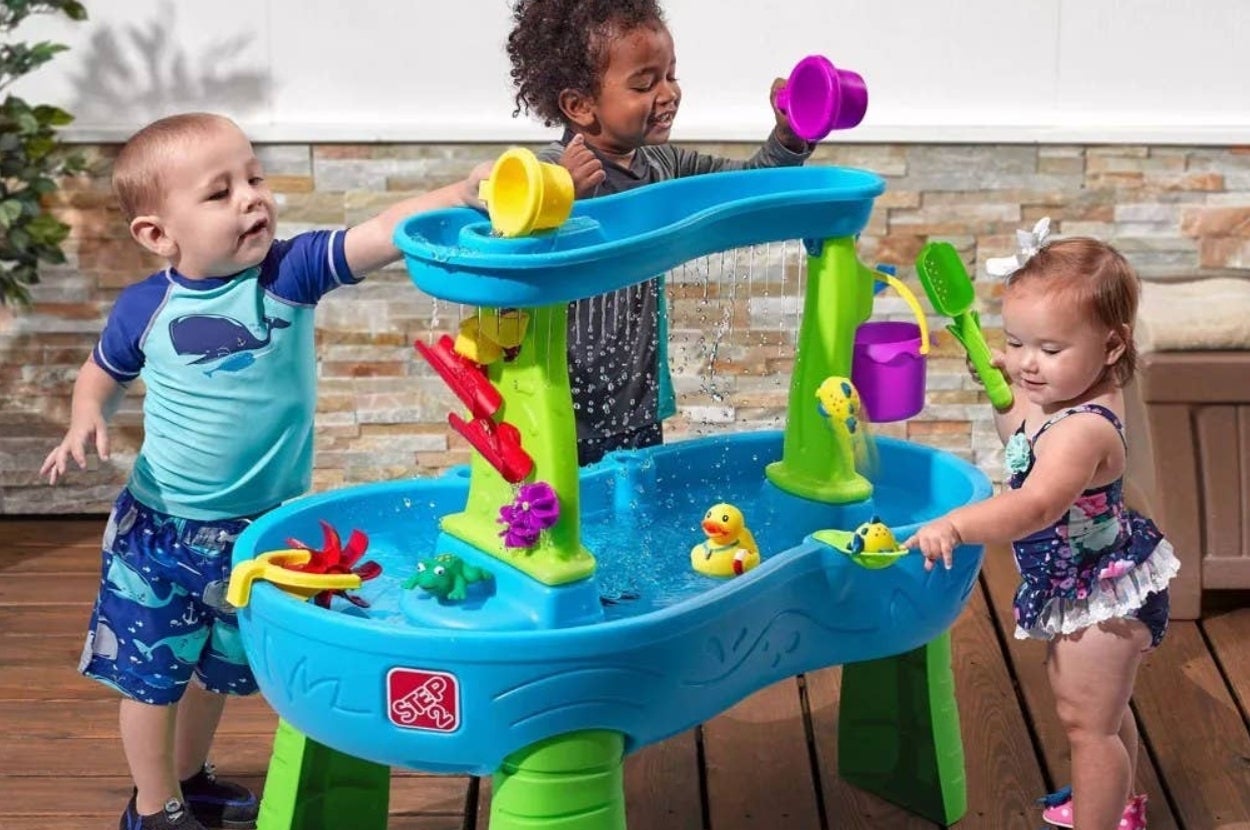 Children playing with a multi-level water table featuring various interactive toys like ducks, a spinner, and a waterfall, encouraging creative play