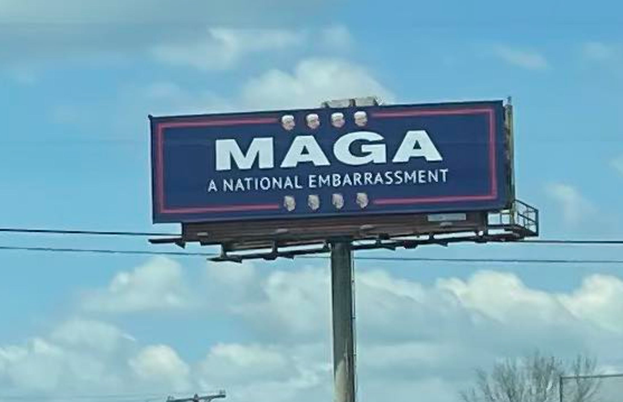 Reklametavle med fet tekst som sier «MAGA A National Embarrassment»," mot klar himmel. Ansikter er justert over og under frasen
